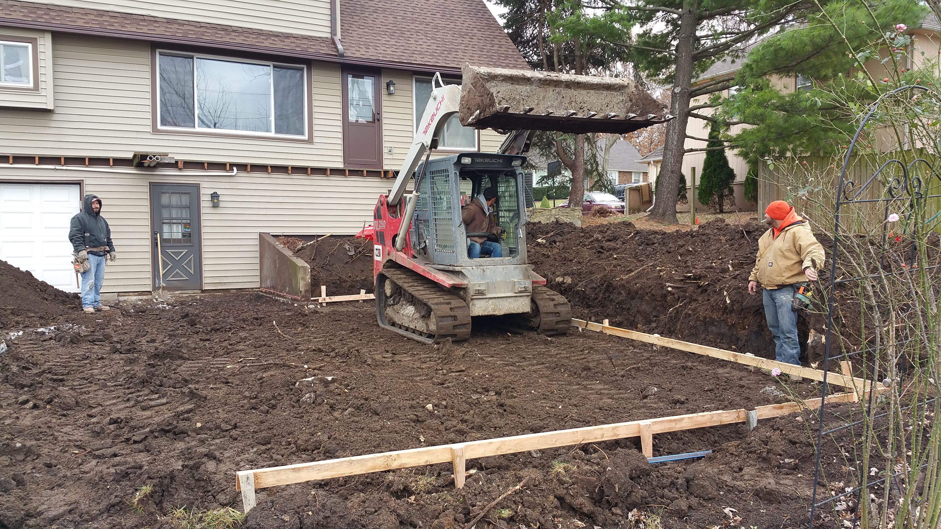 A compact excavator digging soil in a backyard construction site.