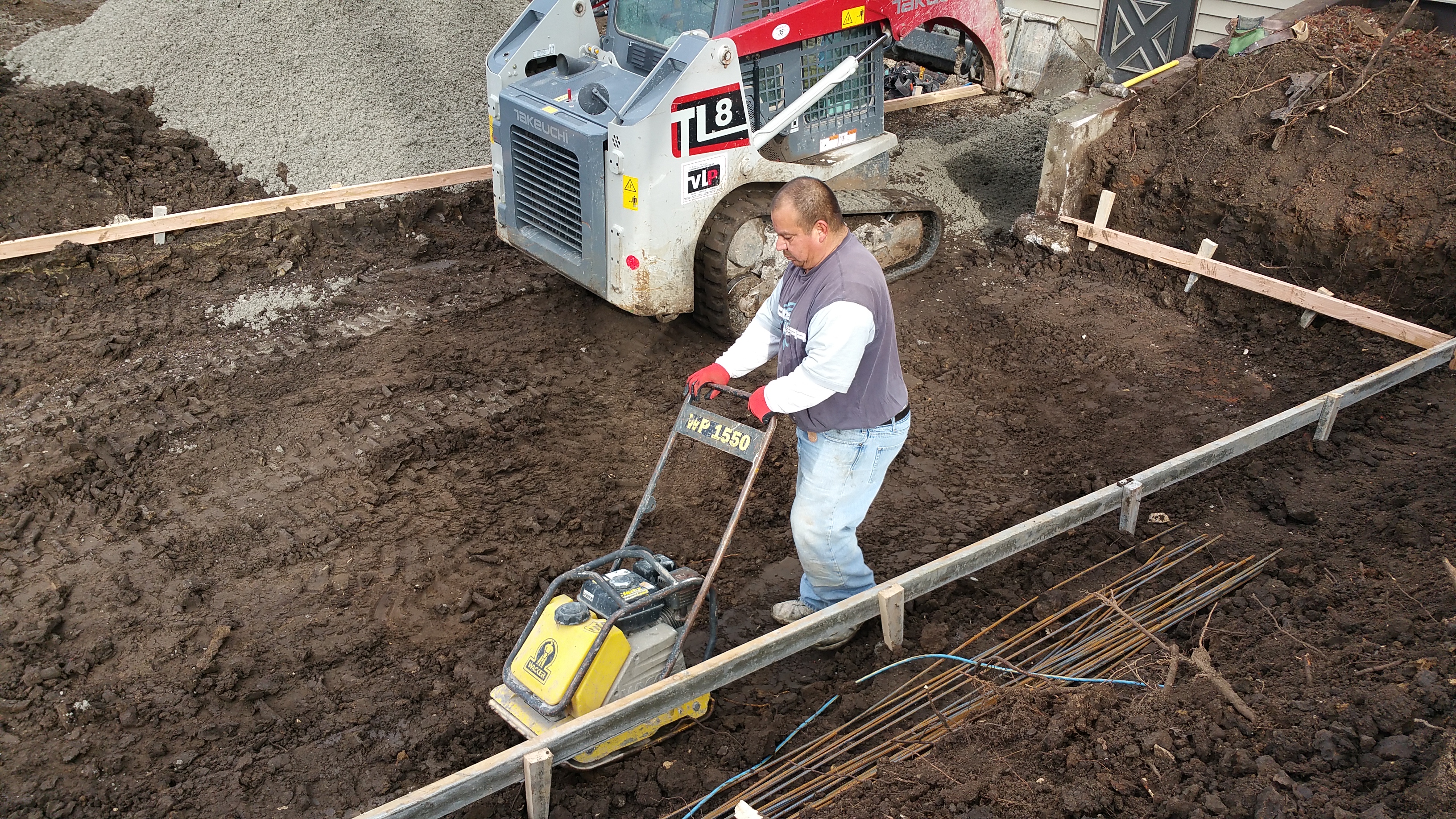 Worker operating a compactor on a construction site with steel reinforcements.