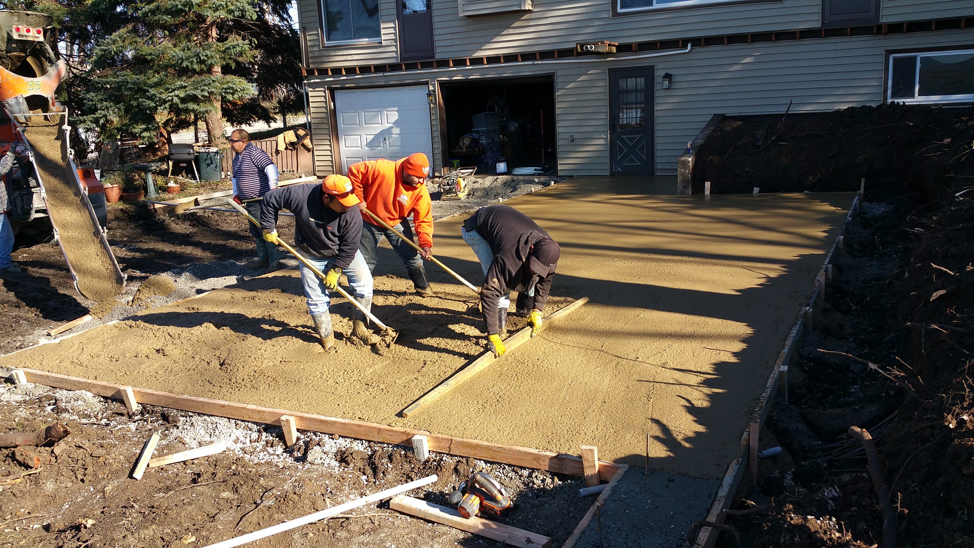 Workers leveling freshly poured concrete outdoors.