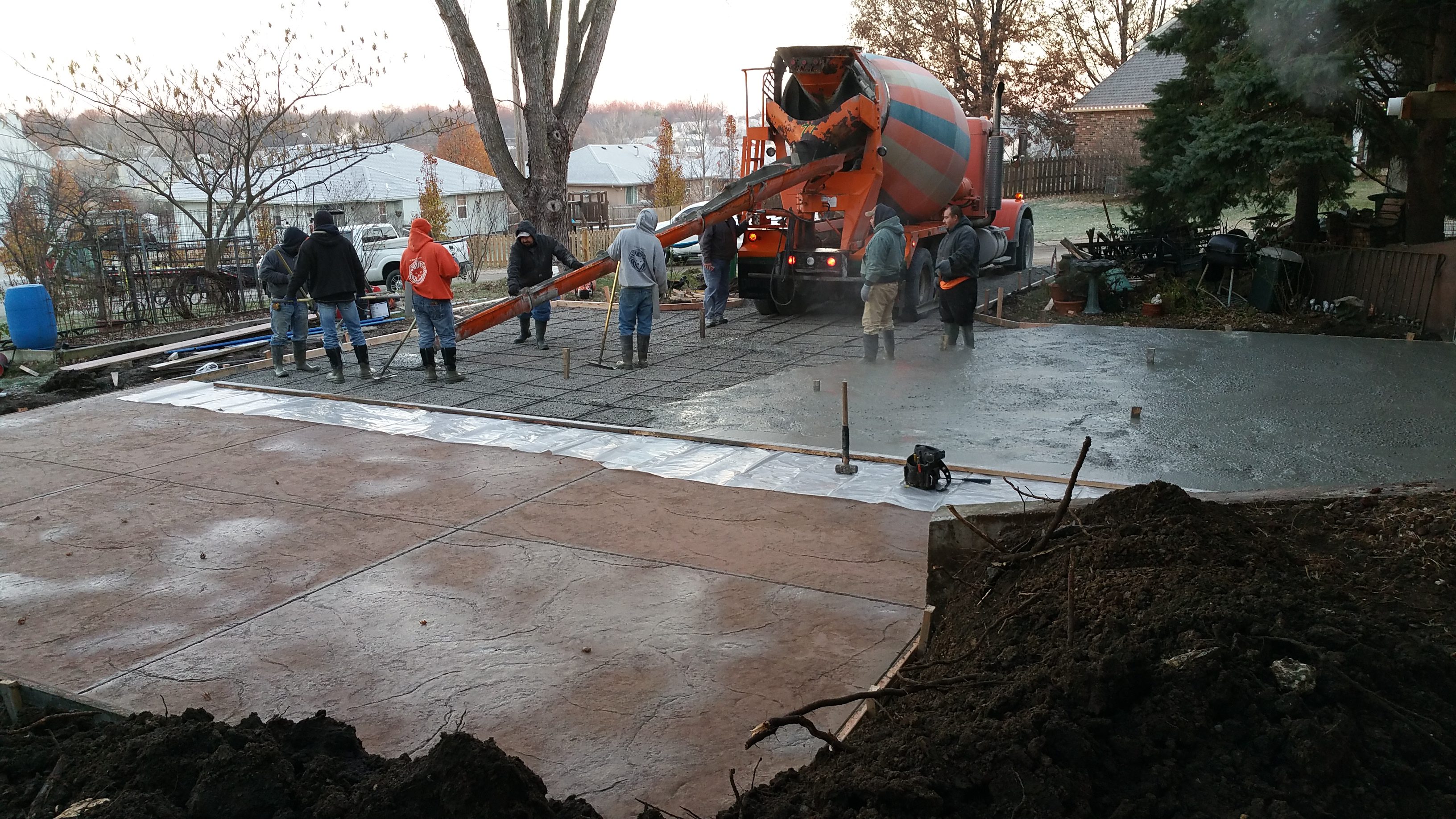 Workers pouring concrete from a mixer onto a prepared surface outdoors.