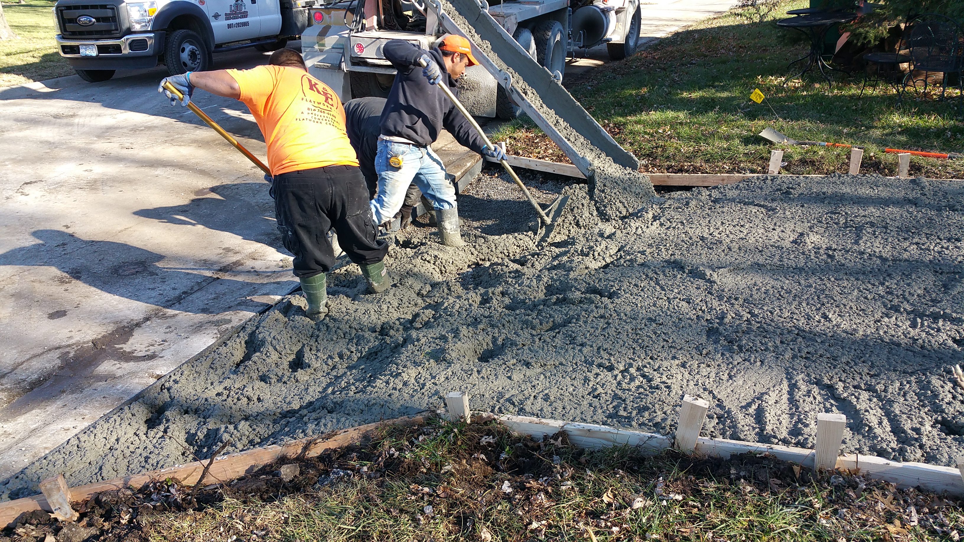 Workers pouring and spreading concrete at a construction site.