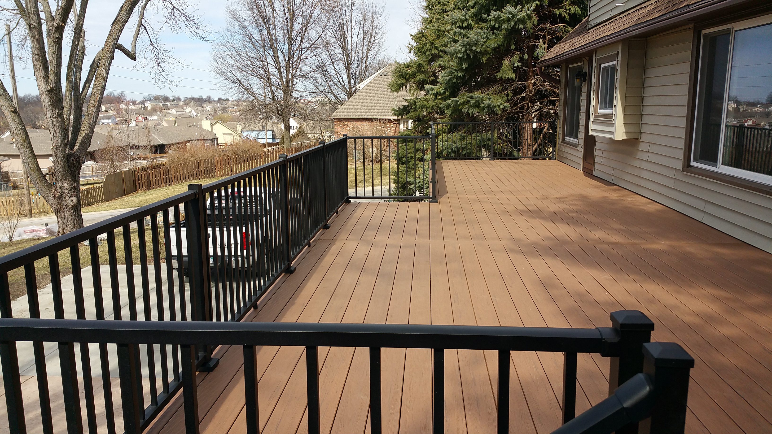Spacious wooden deck with black railings overlooking a backyard.