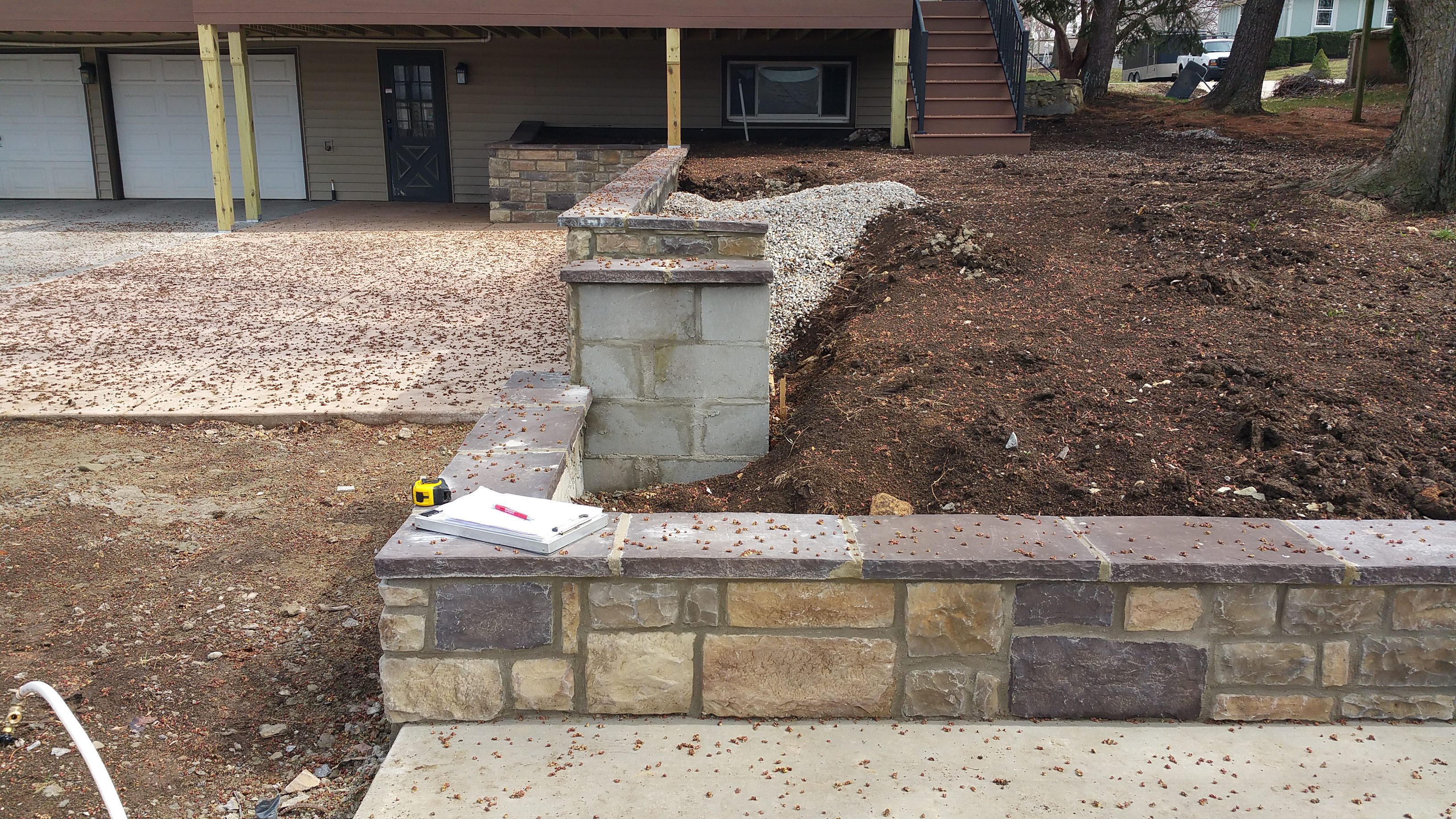 Newly constructed stone wall and landscaping in front of a house.