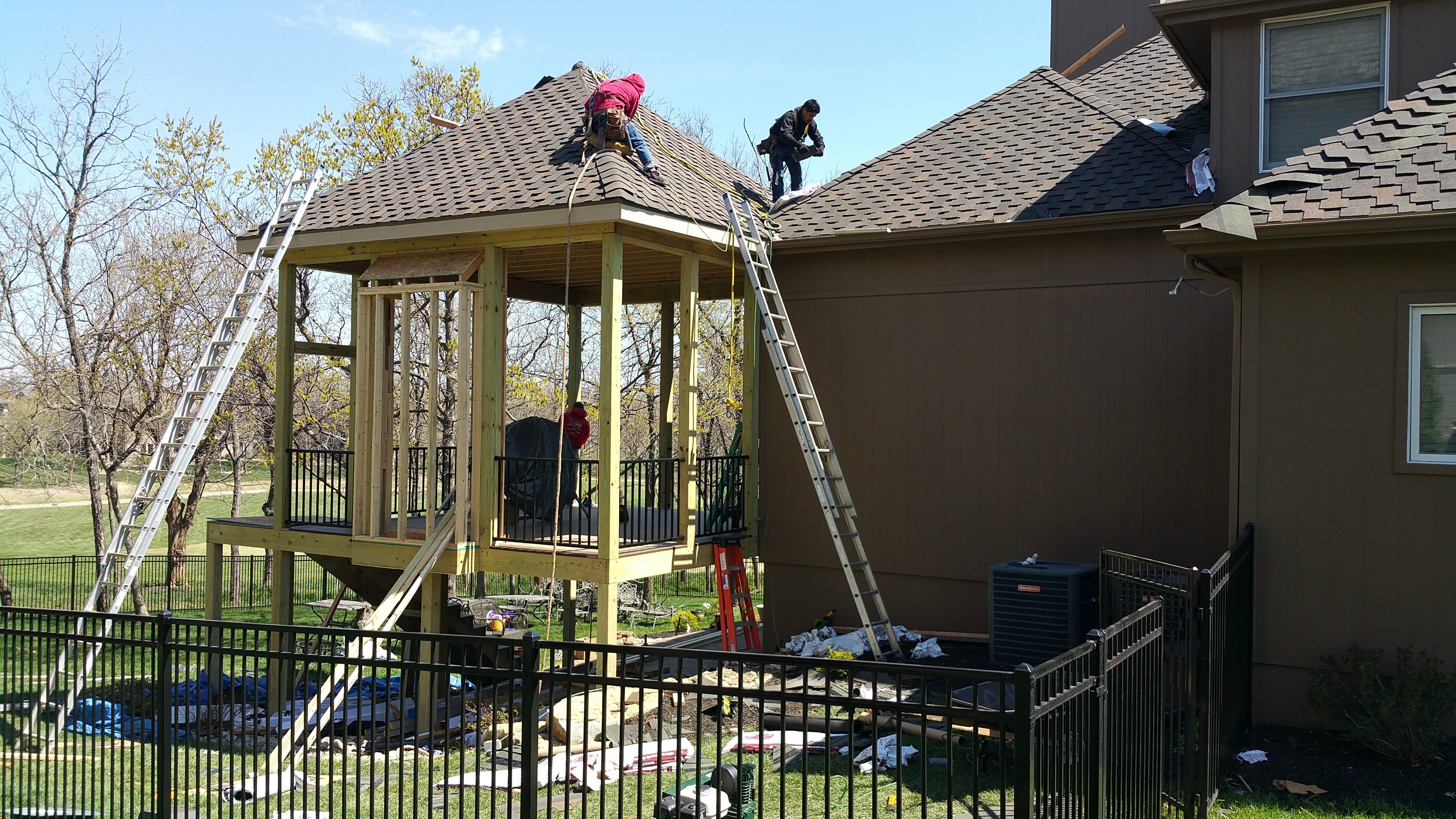 Workers constructing a wooden gazebo in a backyard.