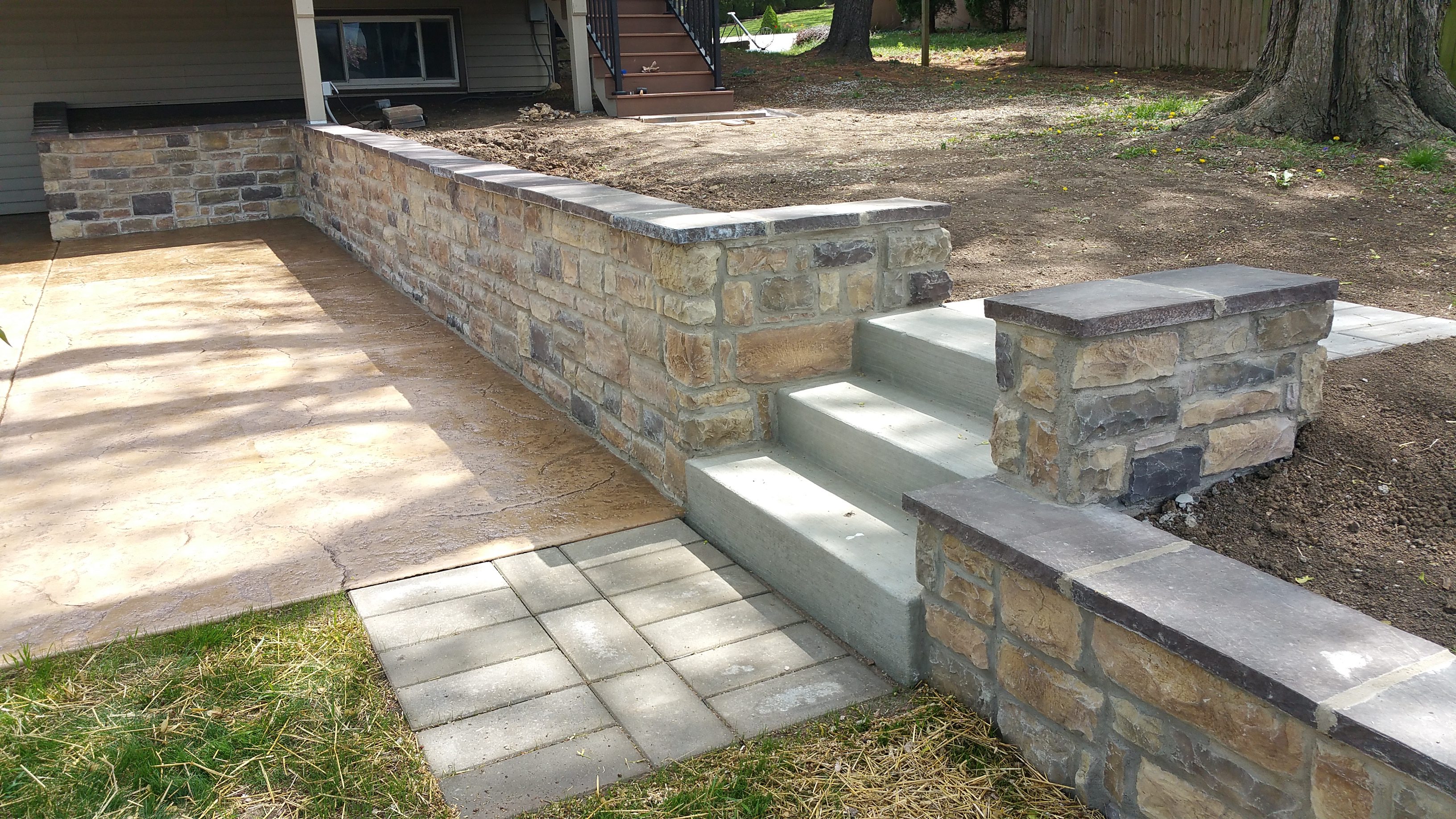 Stone retaining wall with concrete steps and paved walkway.