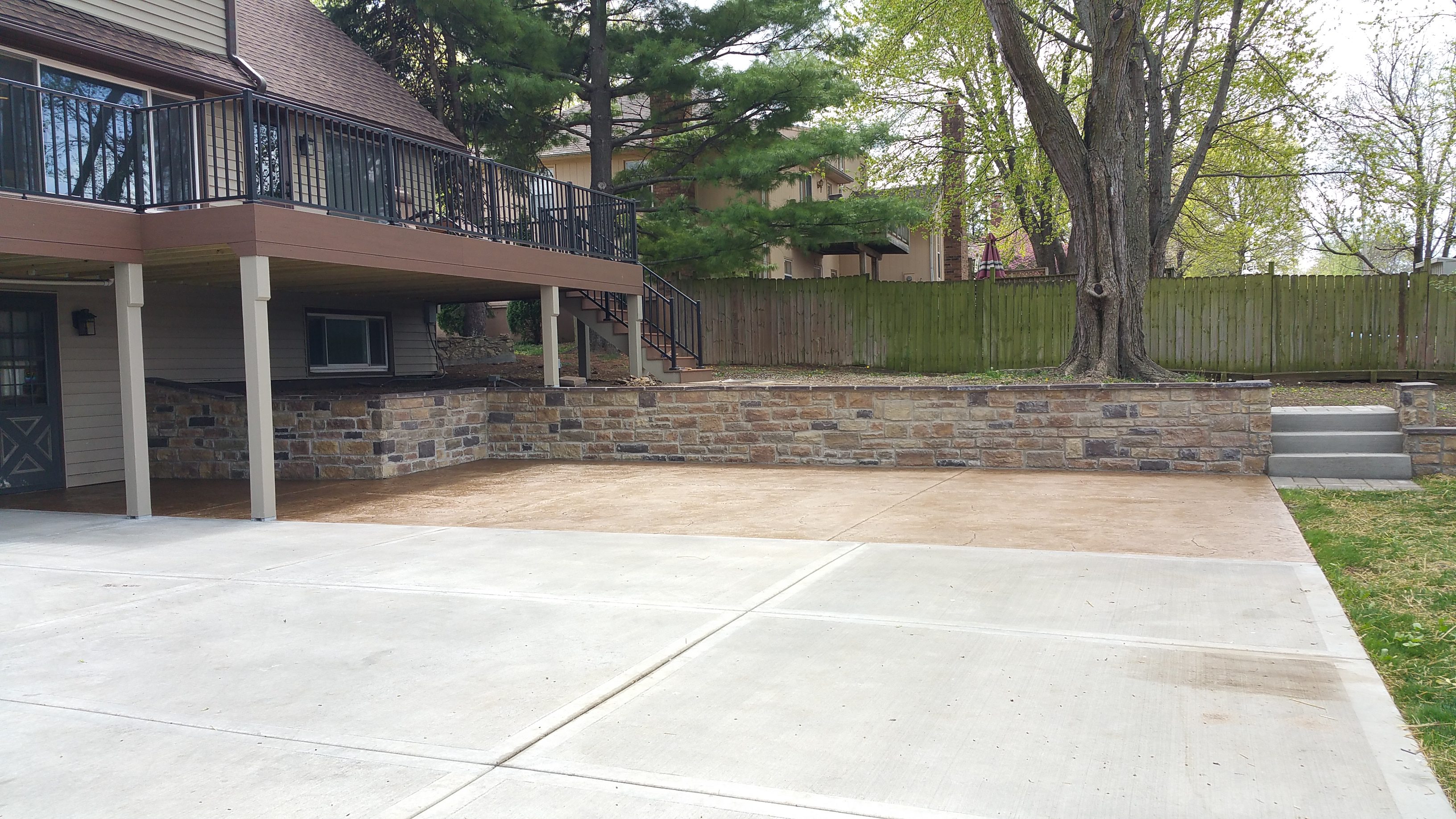 Empty concrete driveway beside a stone retaining wall and trees.