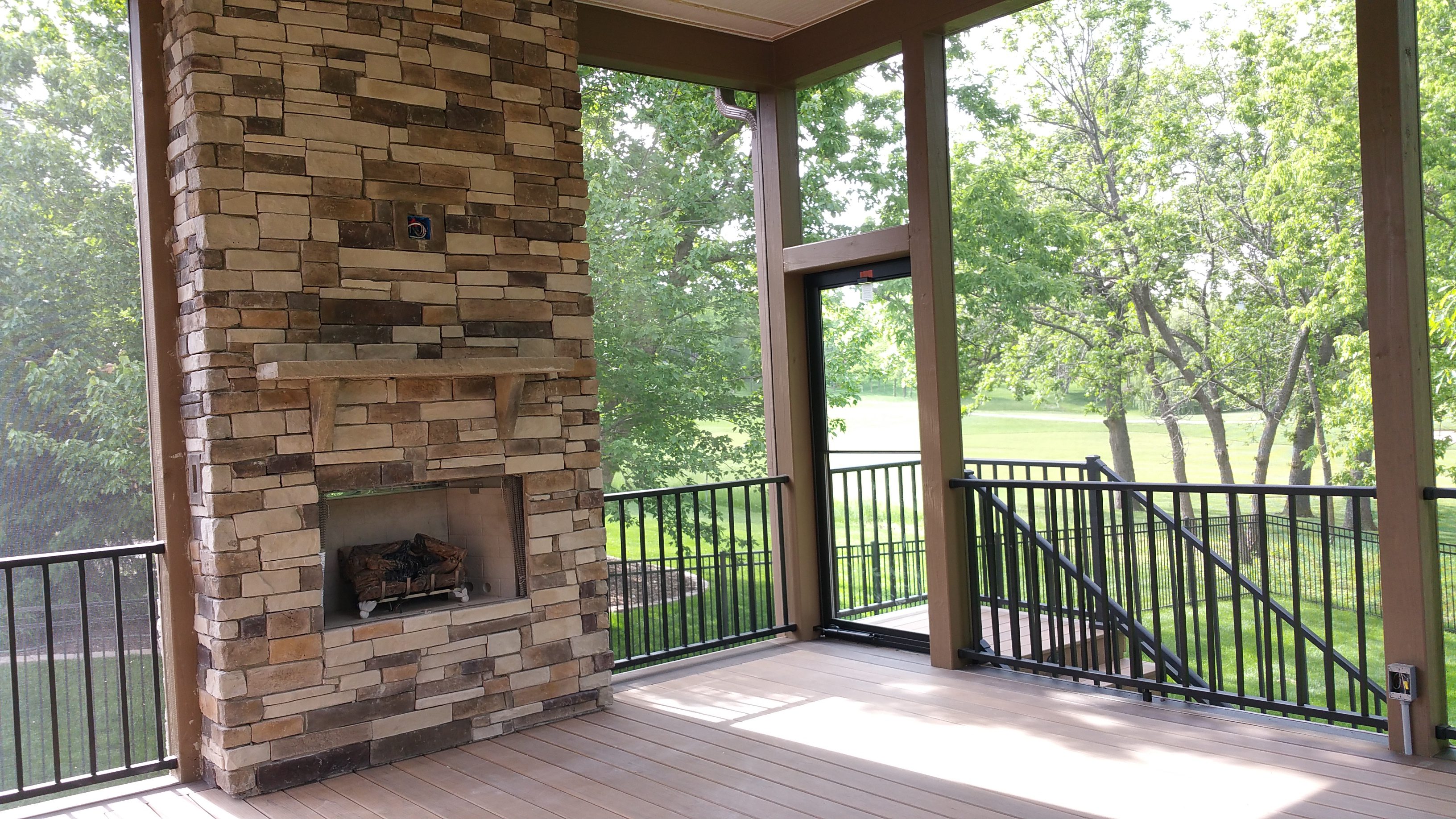 Cozy outdoor patio with stone fireplace and scenic green view.