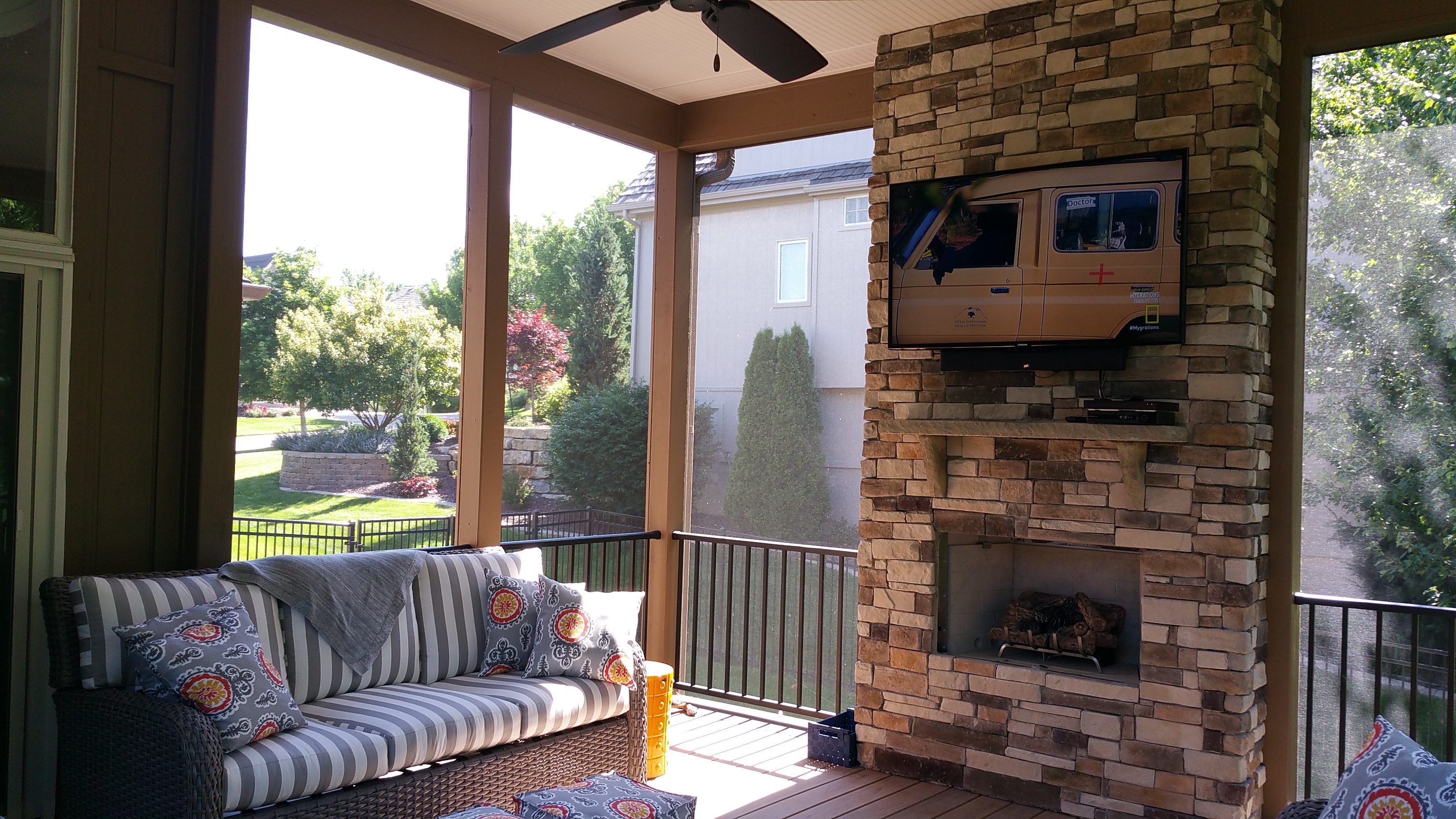 Cozy porch with striped sofa and brick fireplace overlooking a sunny garden.