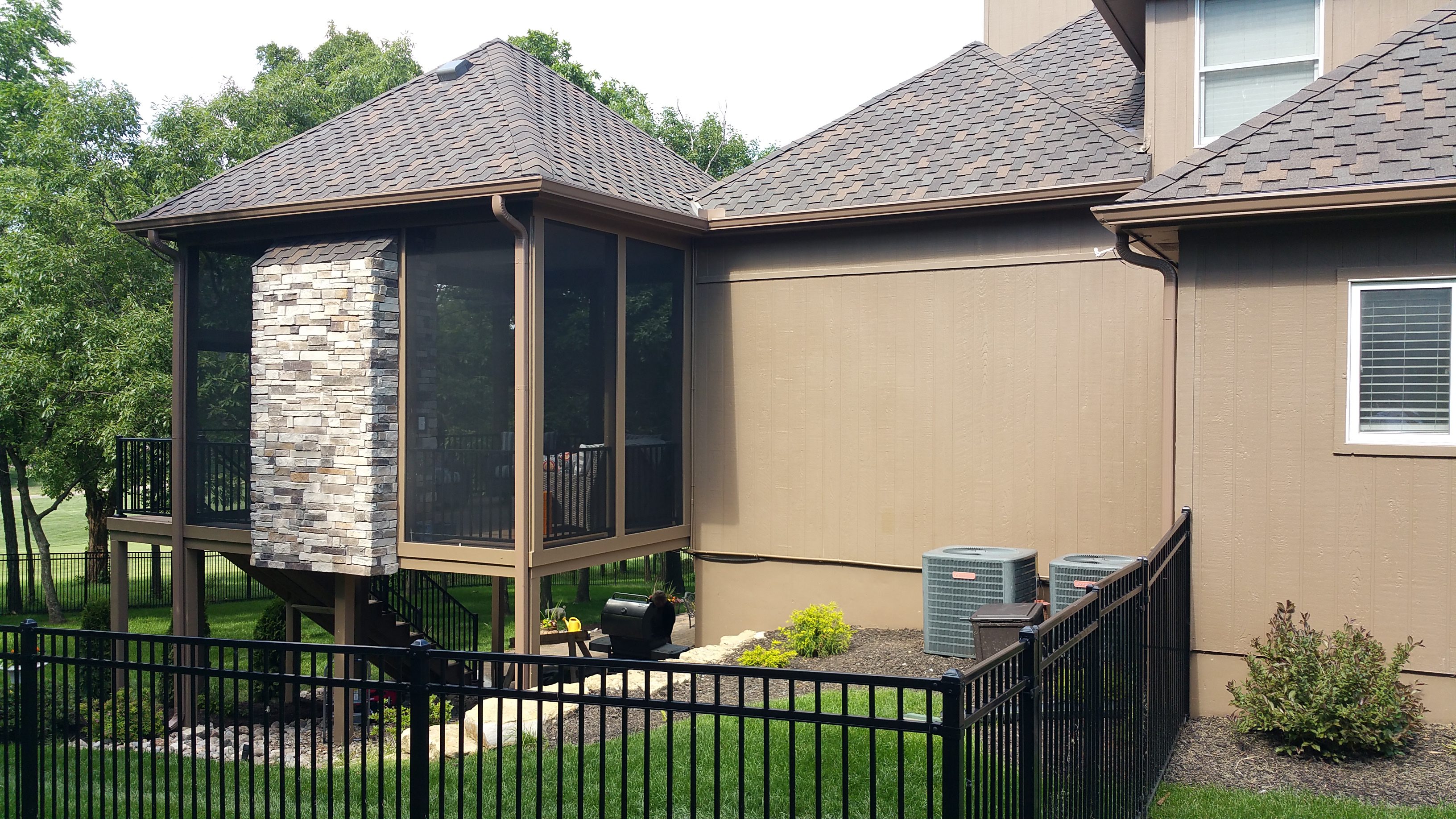 Modern house exterior with stone and beige walls, featuring screened porch and HVAC units.