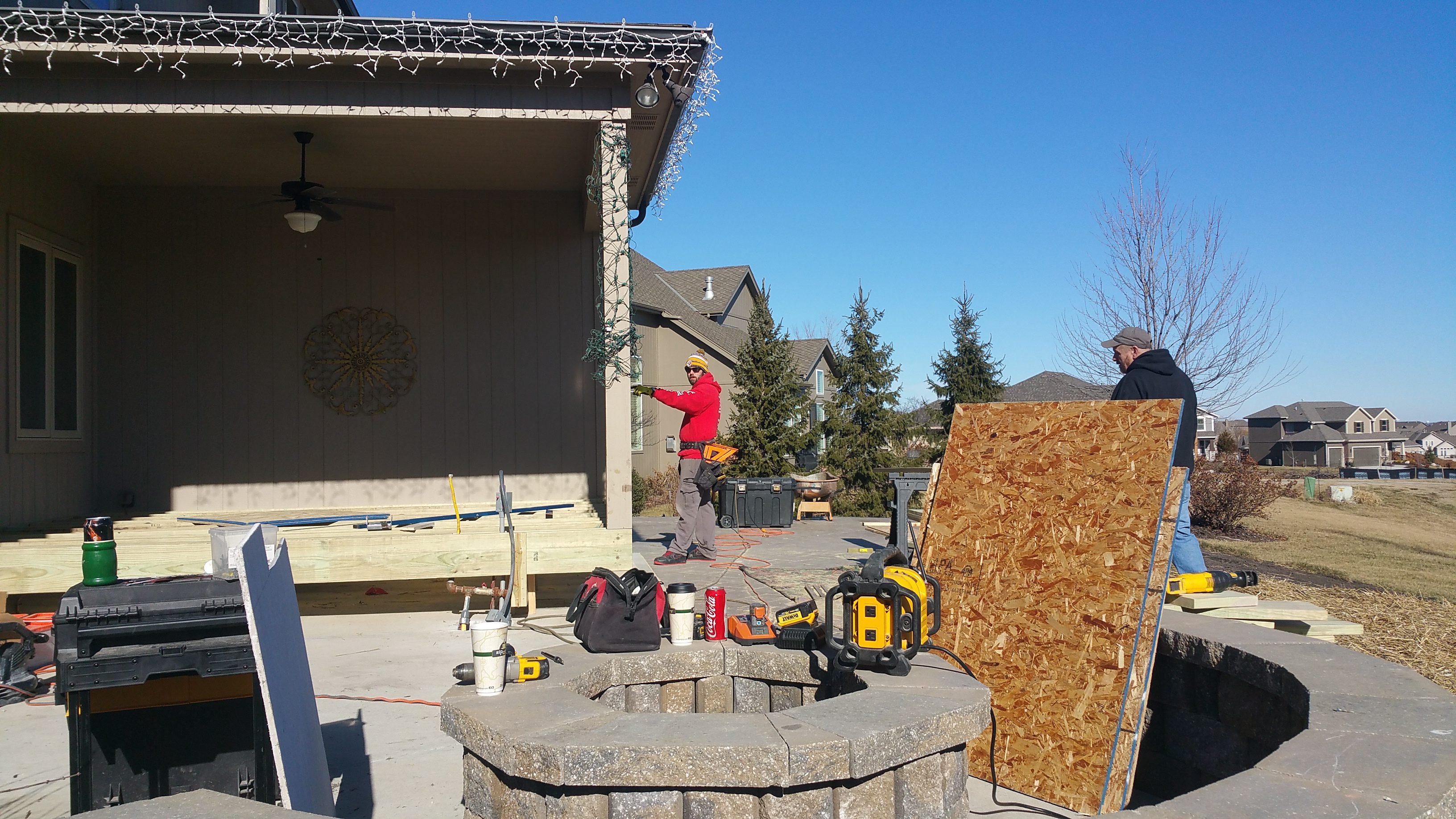 A person working on a roof near a stone fire pit outdoors.