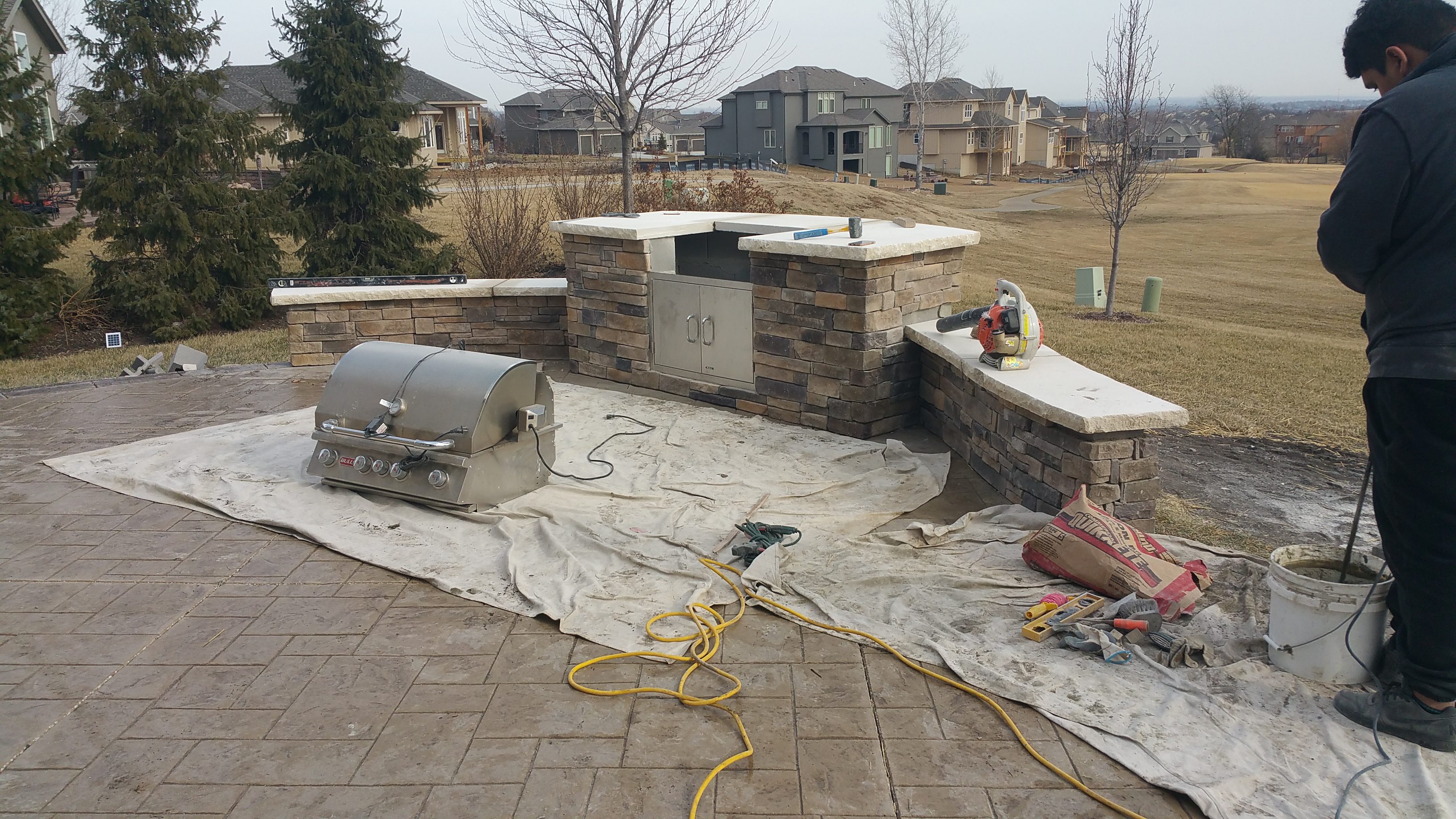 Outdoor grill area with stonework and a grill on a tarp.