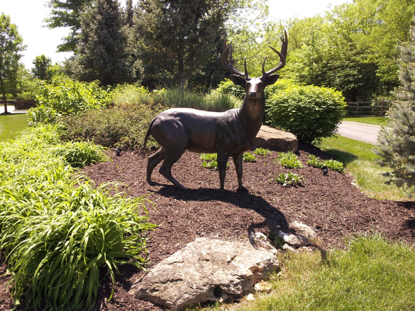 Bronze deer statue in a garden surrounded by greenery.