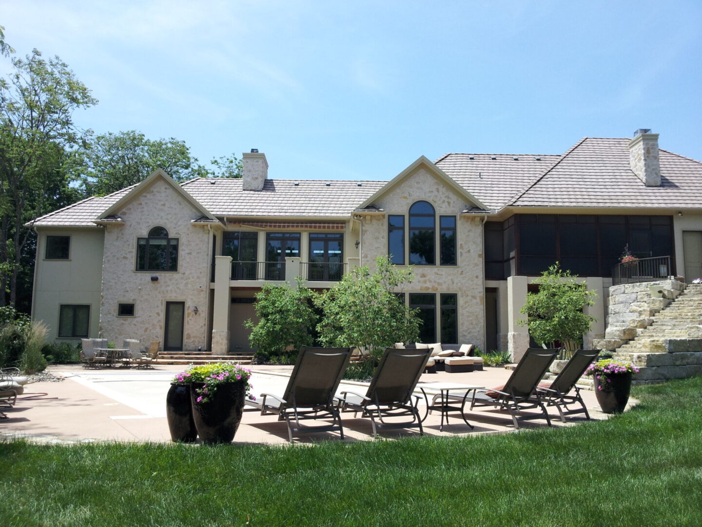 Modern house with a spacious patio and lounge chairs under a clear sky.