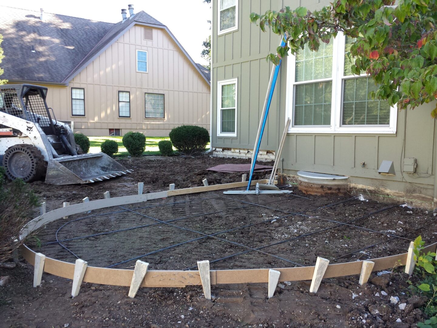 Construction site with wooden framework for concrete pouring near a house.