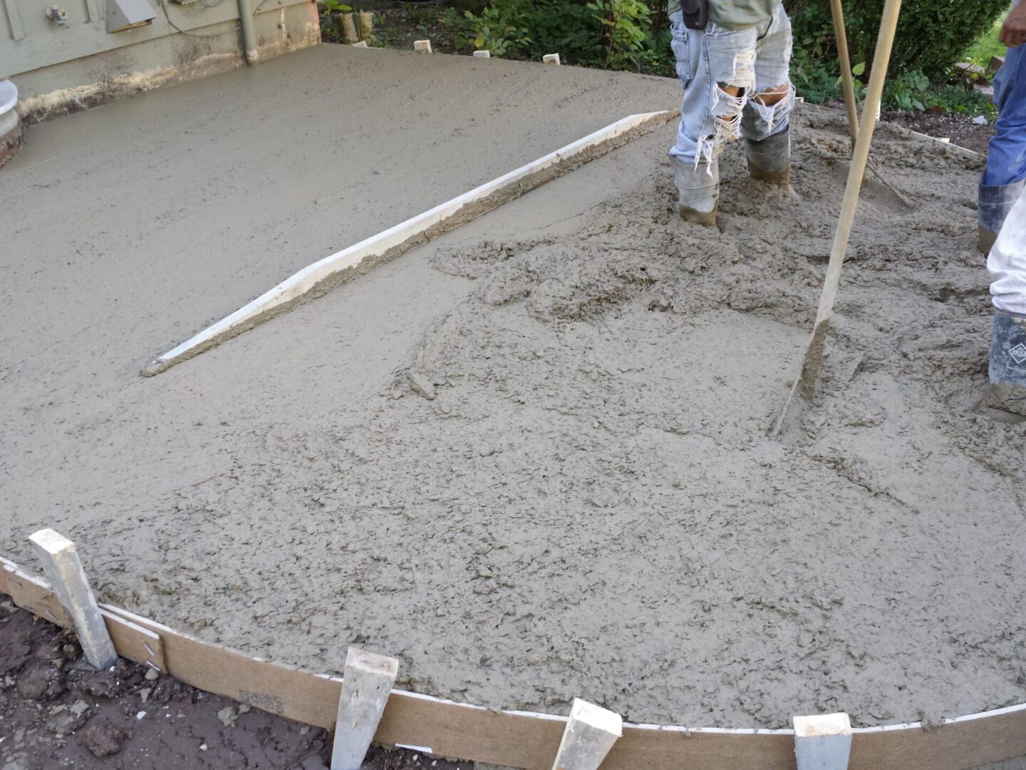 Worker spreading and leveling concrete on a curved surface.