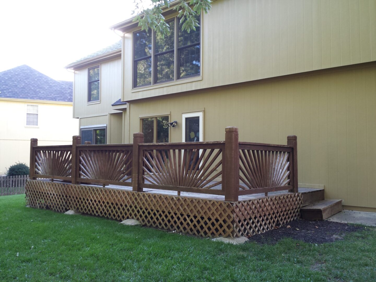 Wooden deck with decorative railing attached to a beige house.