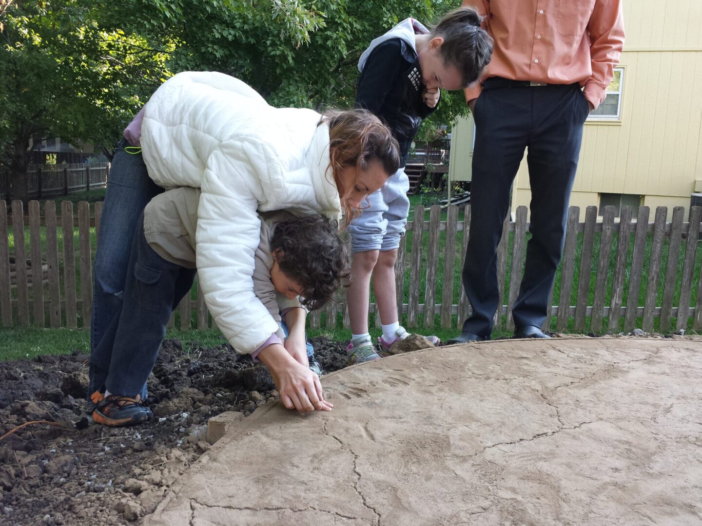 A woman and child drawing on the ground with chalk, watched by an adult.