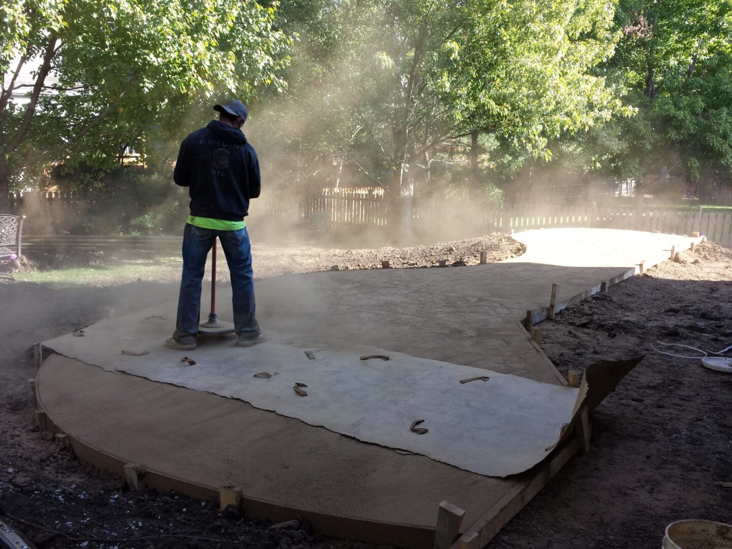 Worker smoothing concrete on a sunny day in a shaded outdoor area.