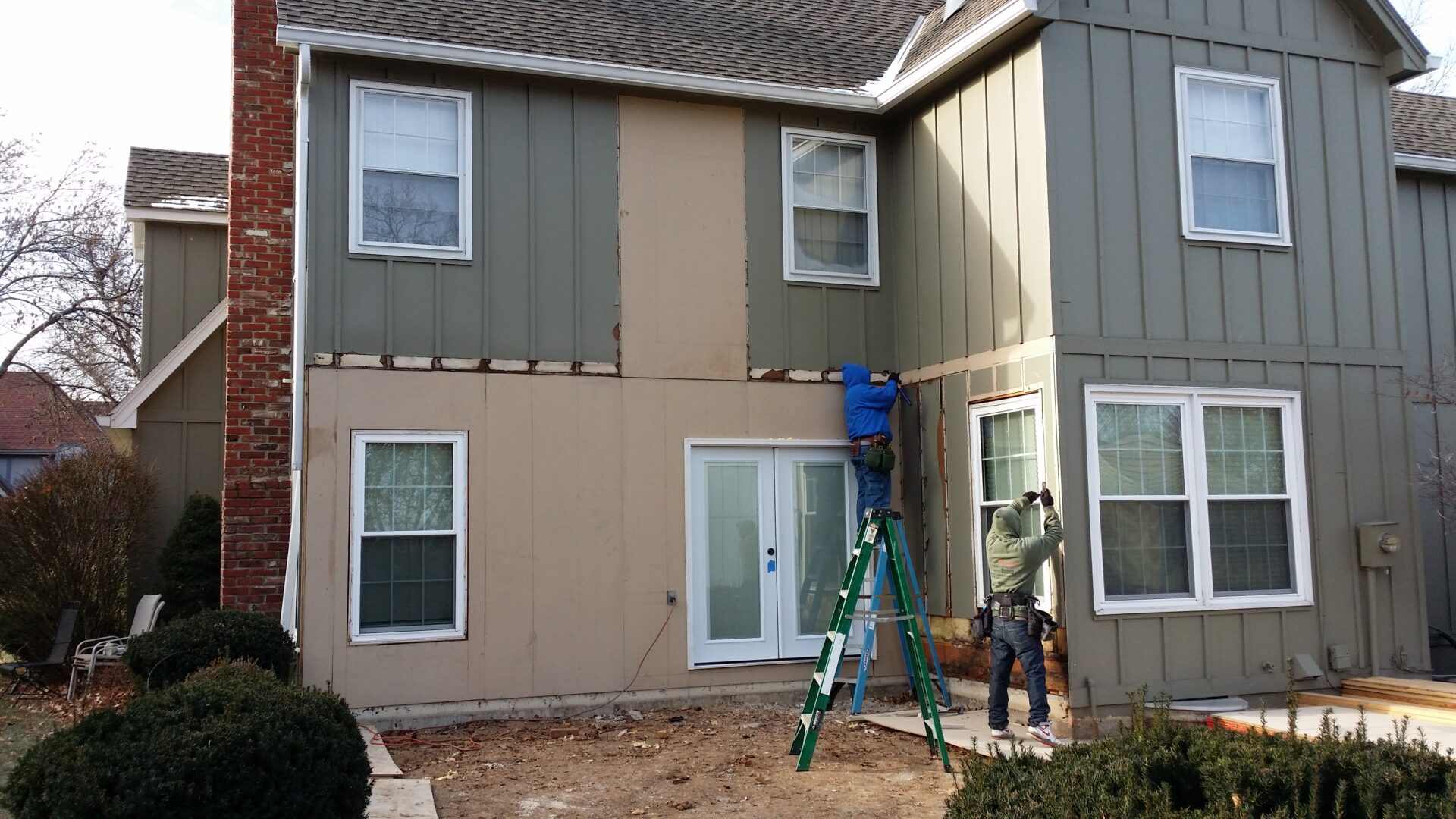 Two workers installing siding on a house exterior with a ladder.