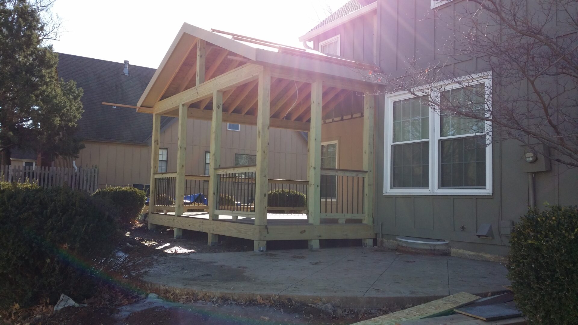 A newly constructed wooden porch attached to a house under bright sunlight.