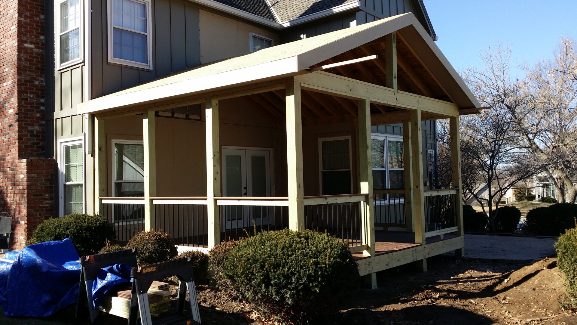 A newly built porch with a roof and screened sides attached to a house.