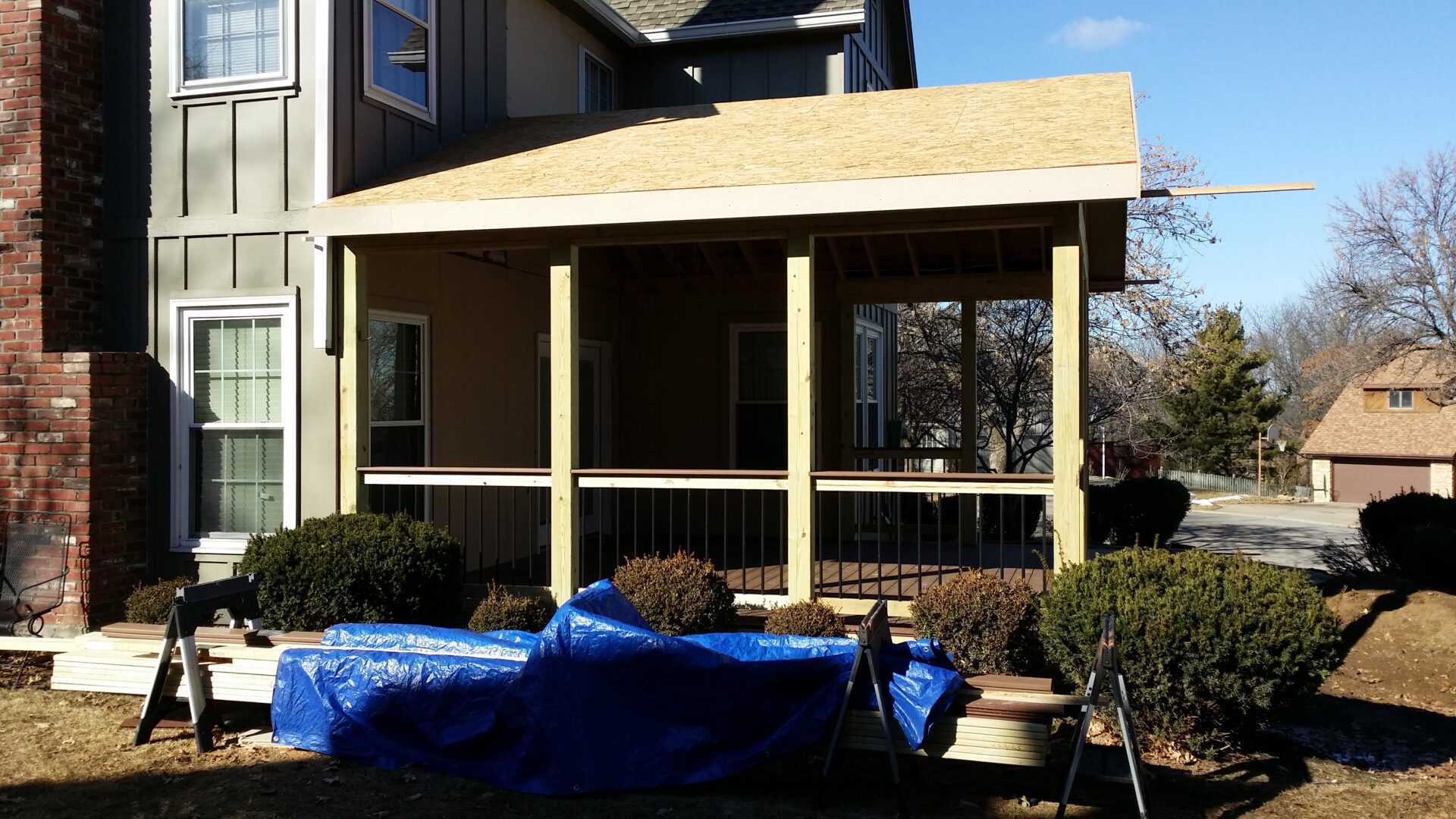 House porch under construction with blue tarp and wooden framework.