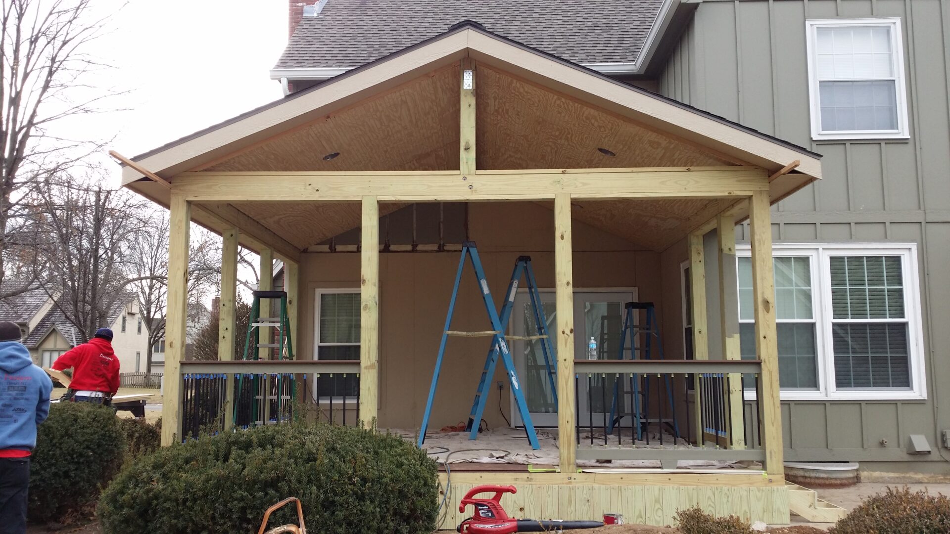 A partially constructed porch with ladders and tools in front of a house.
