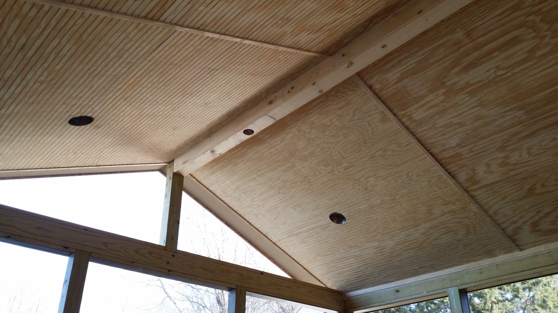 Wooden ceiling with beams and a light fixture in an indoor space.