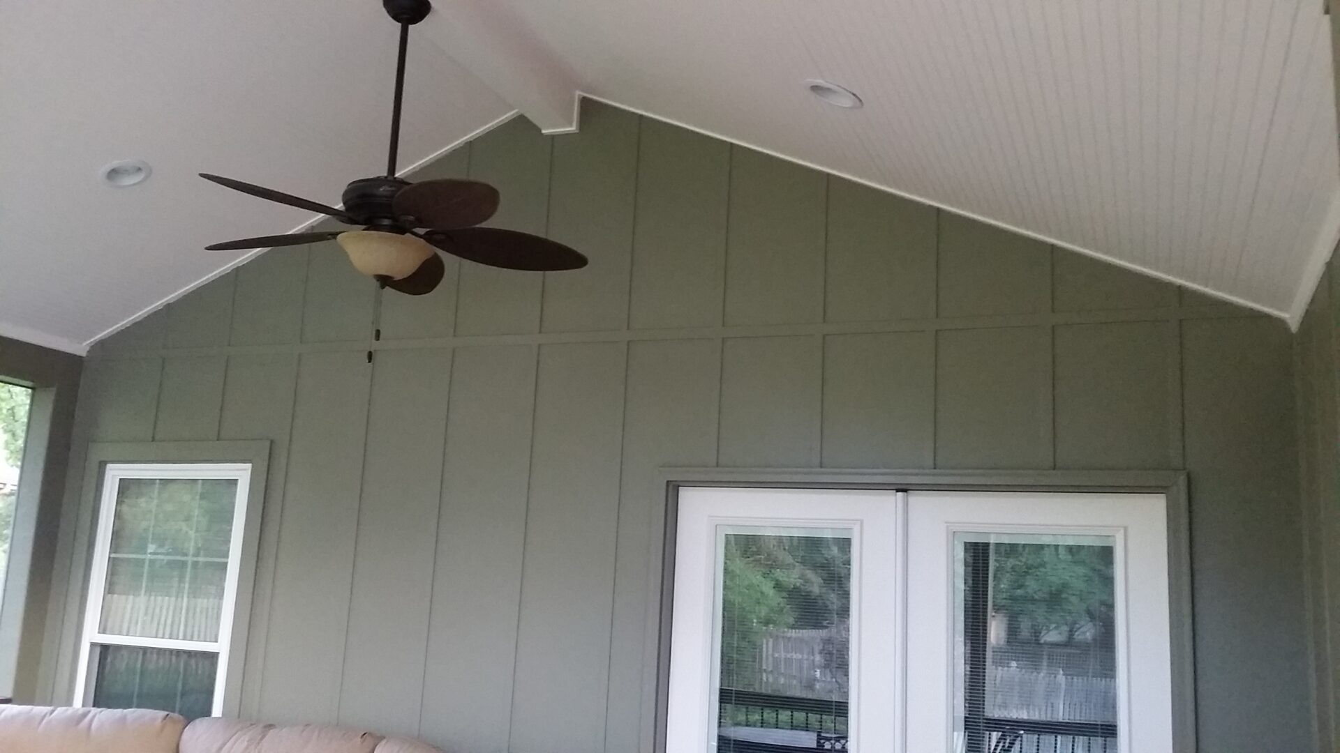 Ceiling fan and double doors on a covered patio with green siding.
