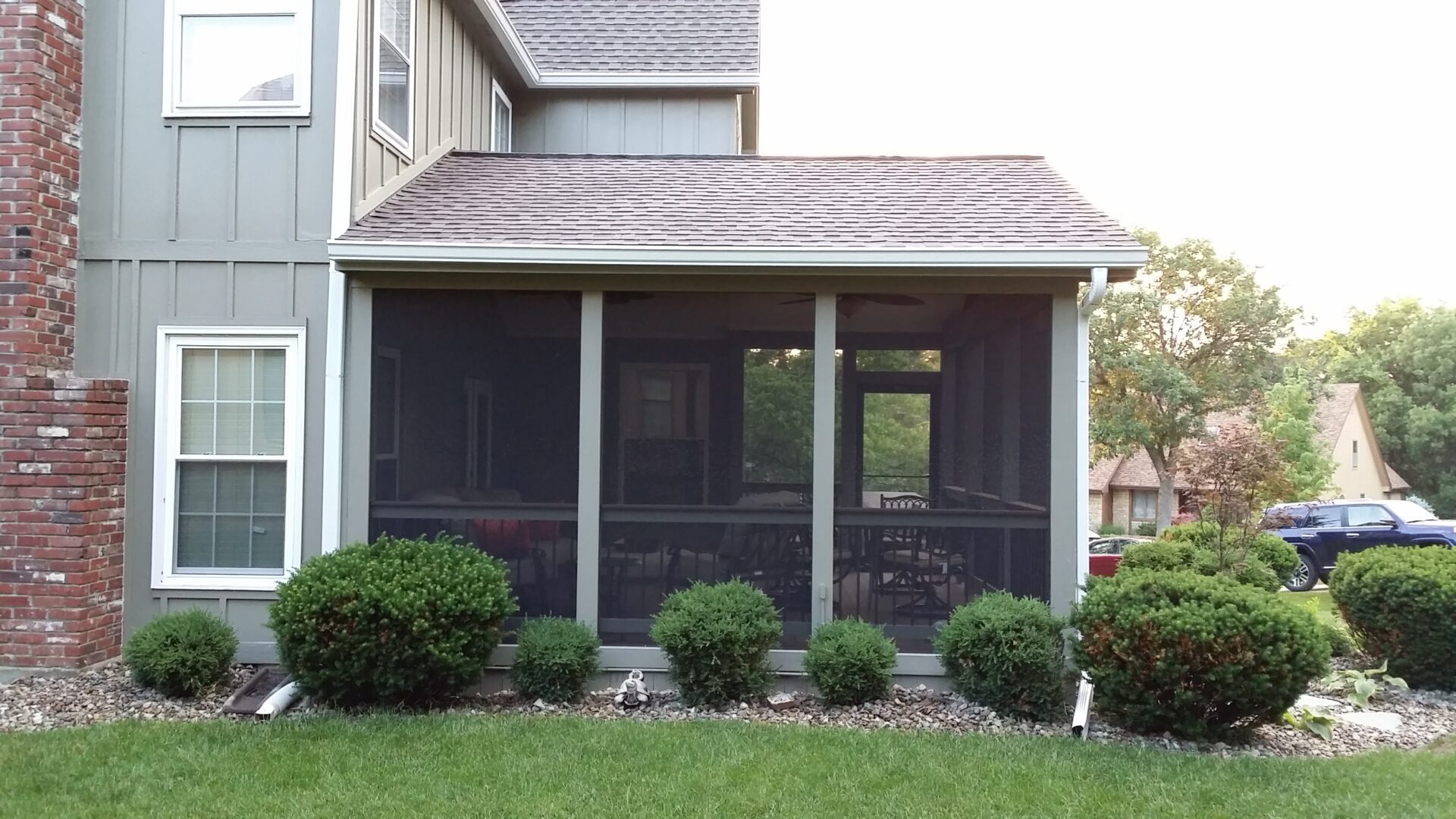 Screened-in porch attached to a house with shrubbery in front.
