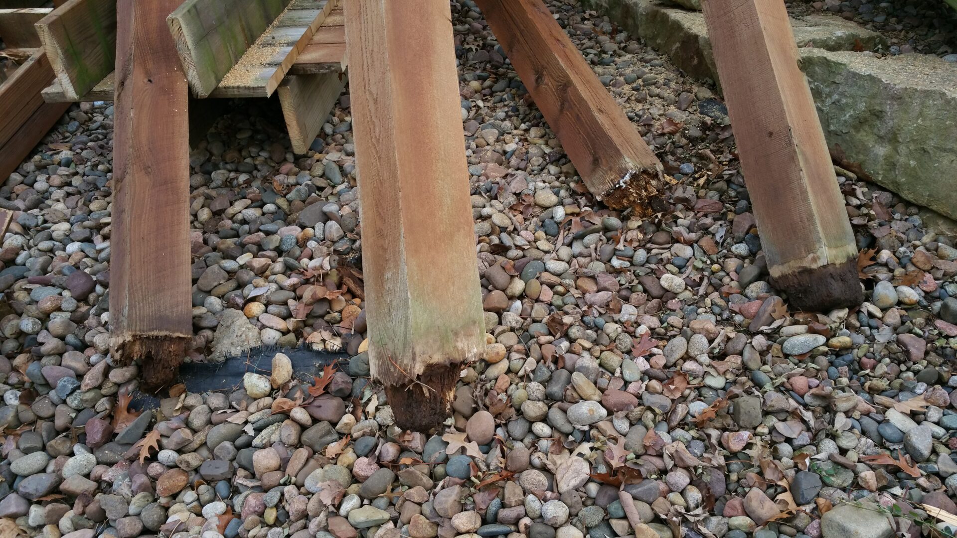 Wooden beams resting on a bed of small rocks outdoors.
