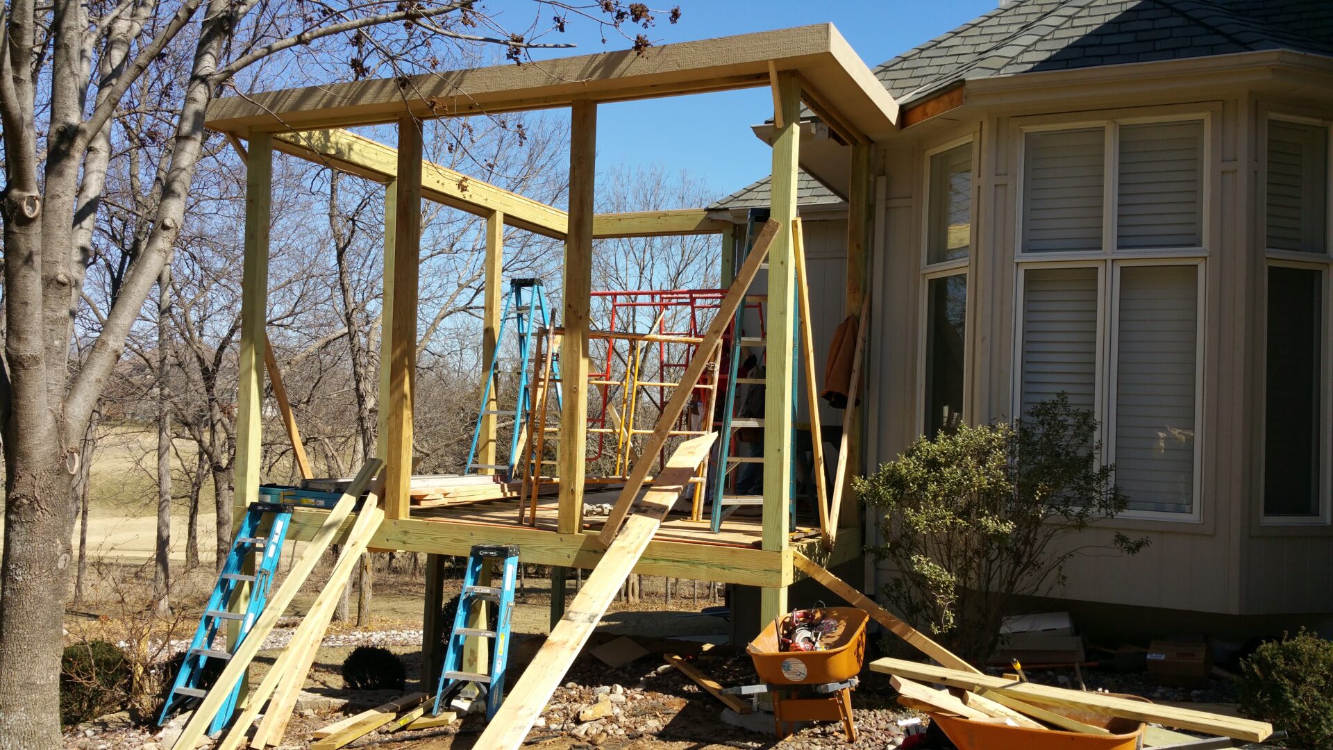 Wooden frame structure being built outside a house on a sunny day.