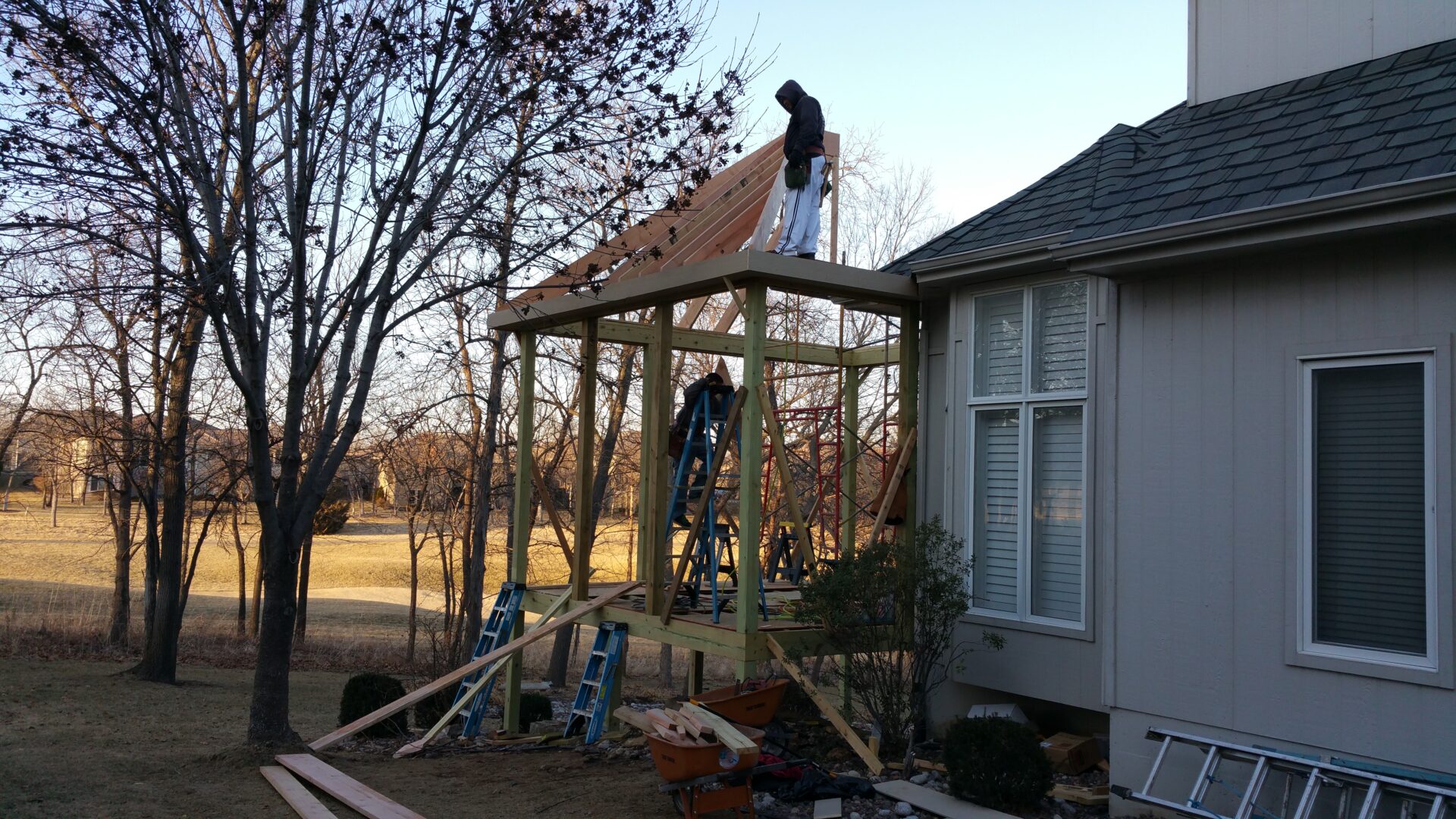 Two people constructing a roof frame beside a house.