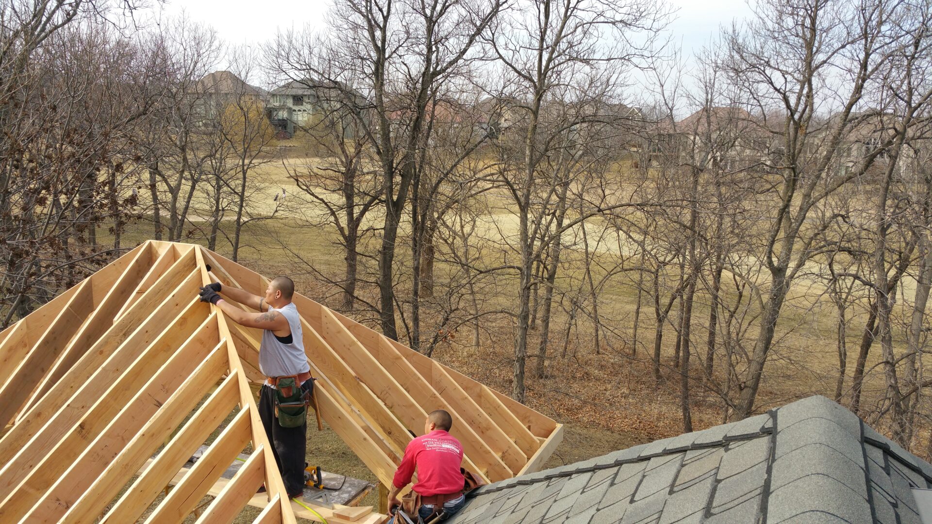 Two workers building a wooden roof frame in a wooded area.