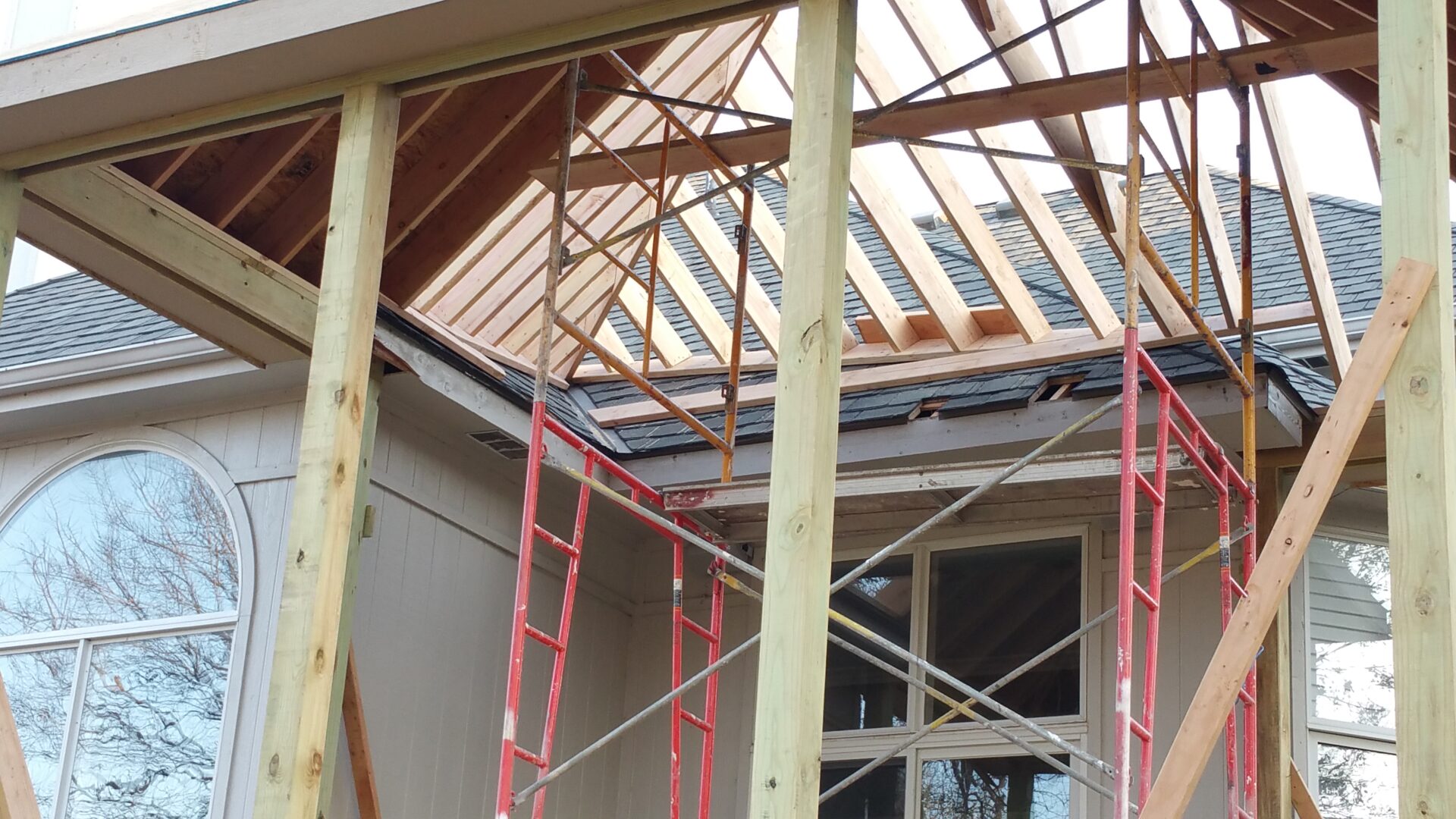 Construction site with wooden framing and scaffolding for a roof installation.