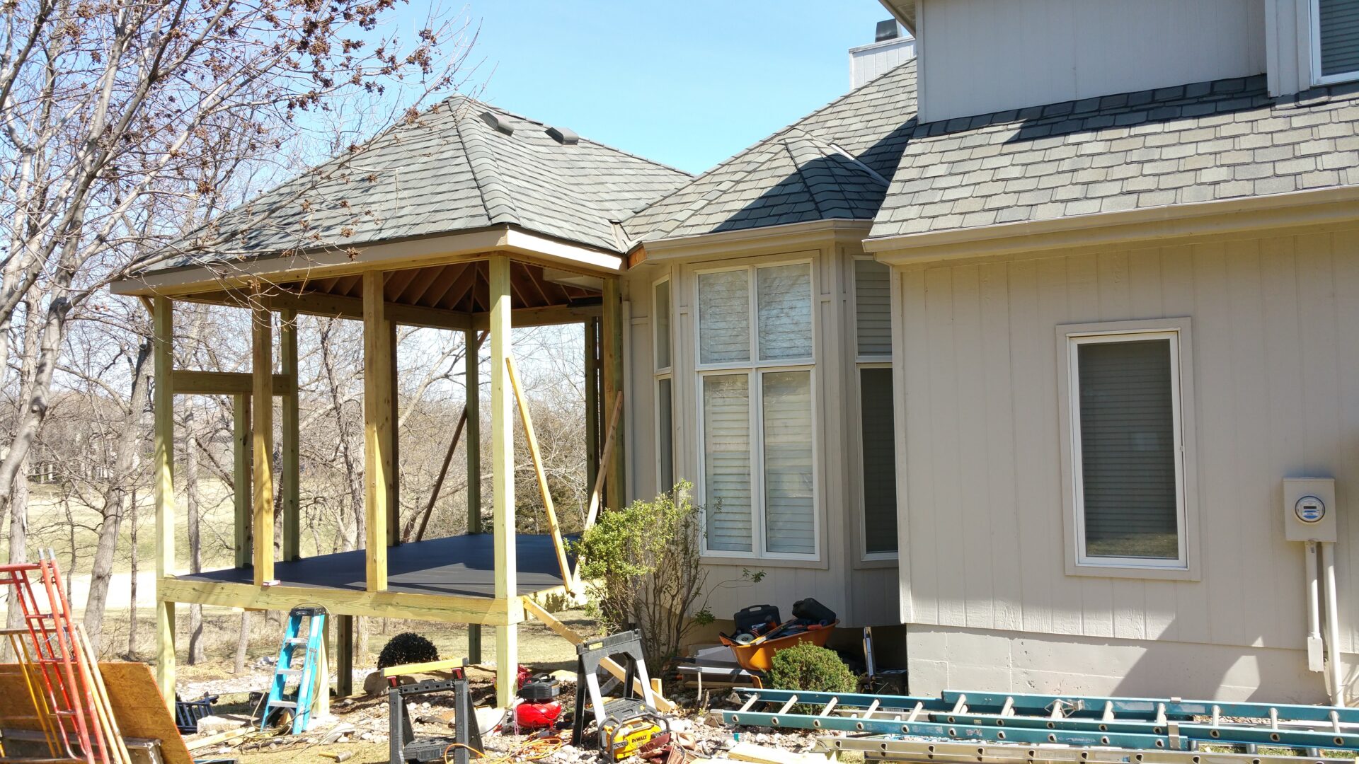 Workers on scaffolding repair a house's exterior near a bay window.