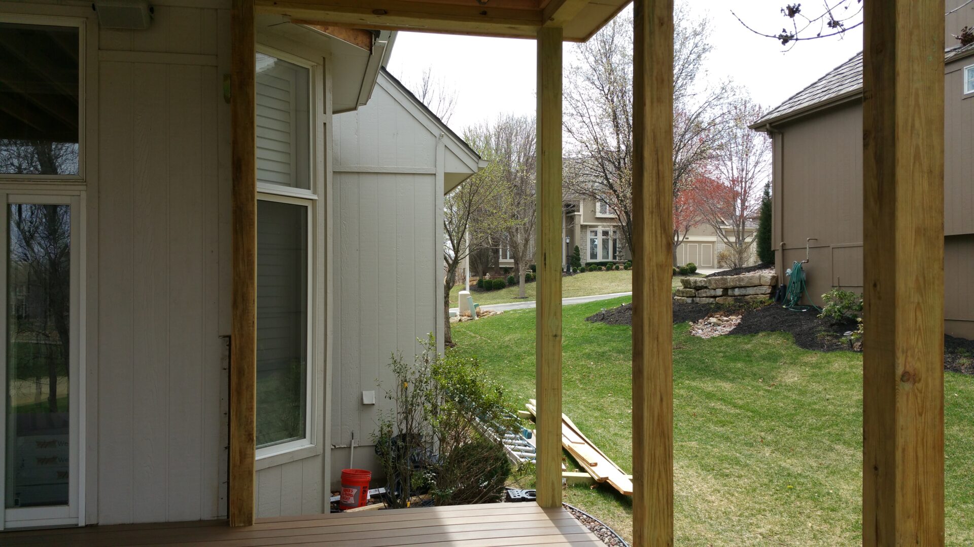 View through a porch showing a grassy yard and neighboring houses on a cloudy day.