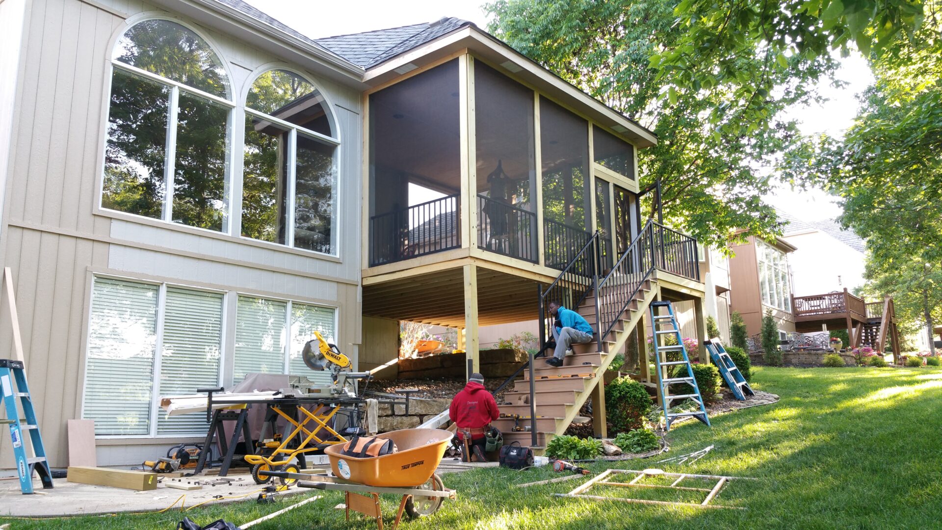 People working on the wooden stairs of a screened porch extension.