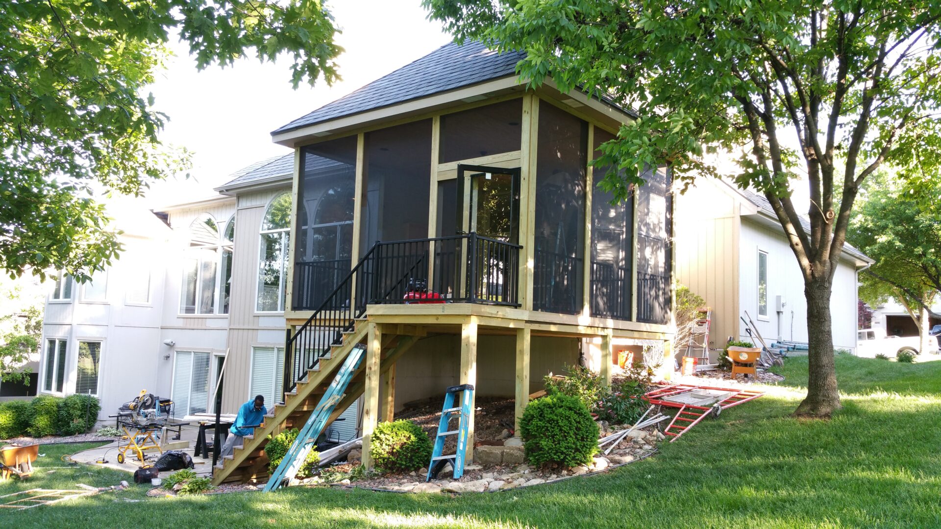 A raised screened porch attached to a house with steps leading down to the yard.