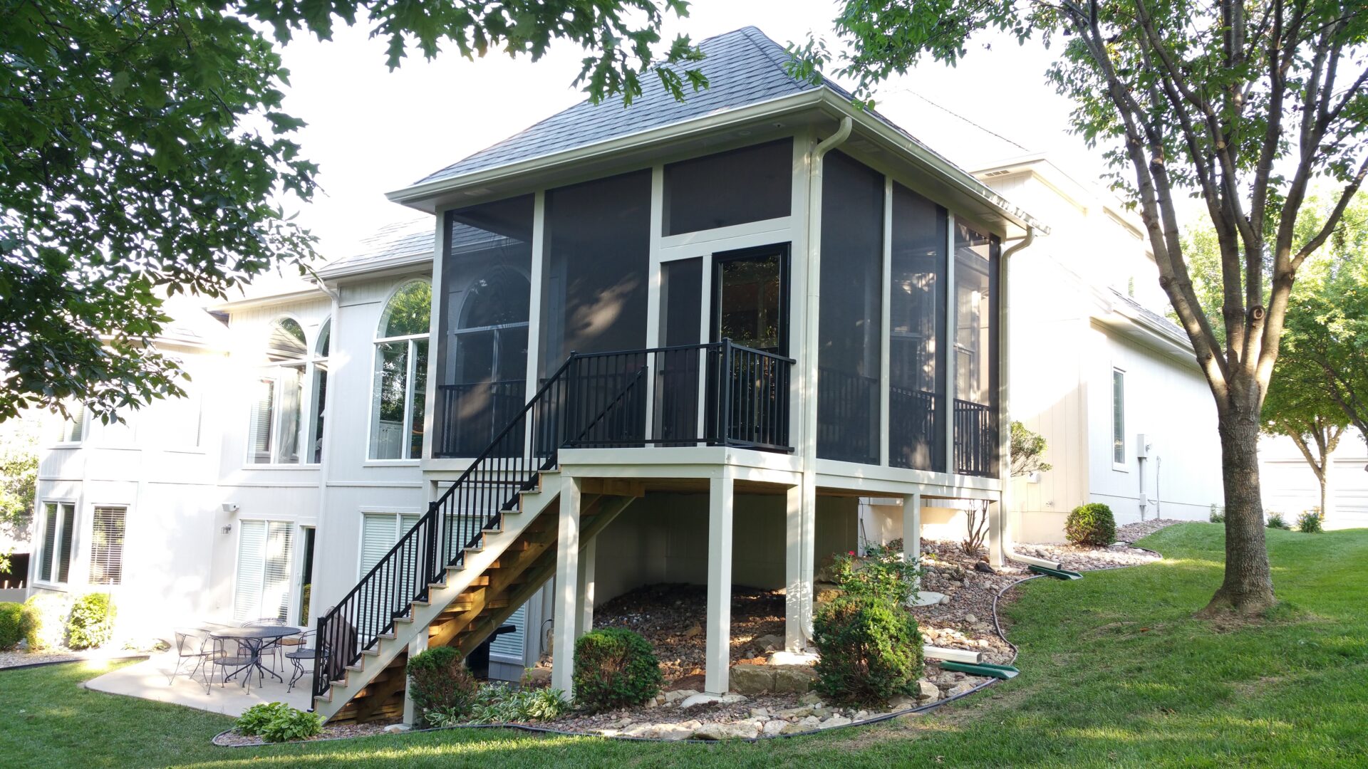 A raised screened porch with stairs leading down to a garden area.