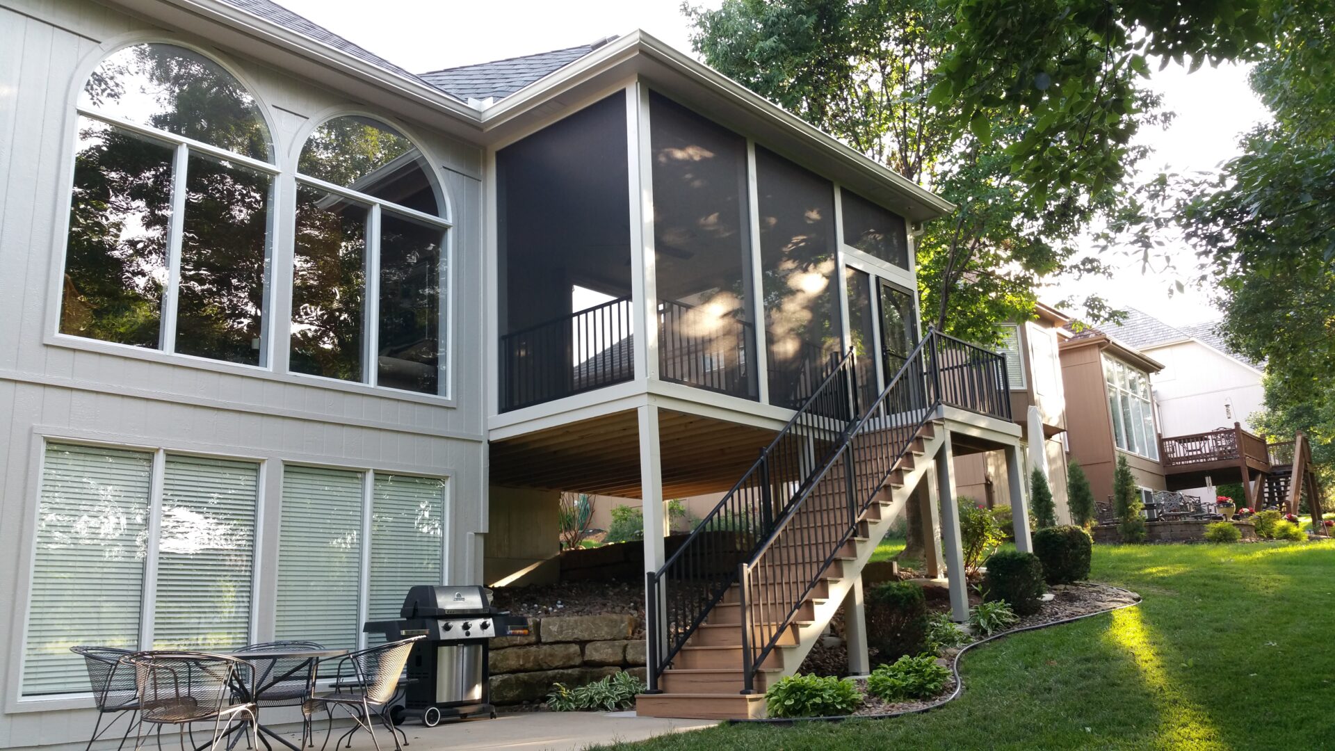 A screened porch with stairs leading down to a backyard patio area.