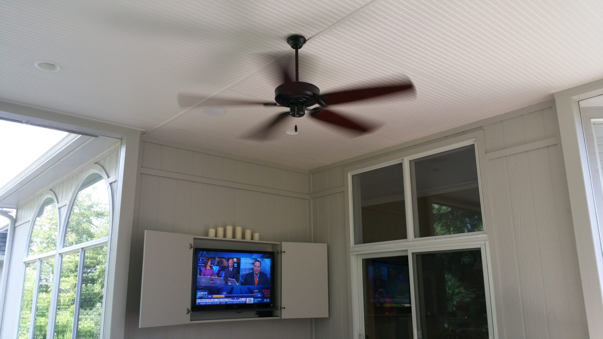 Ceiling fan spinning above a TV on a wall in a cozy room.
