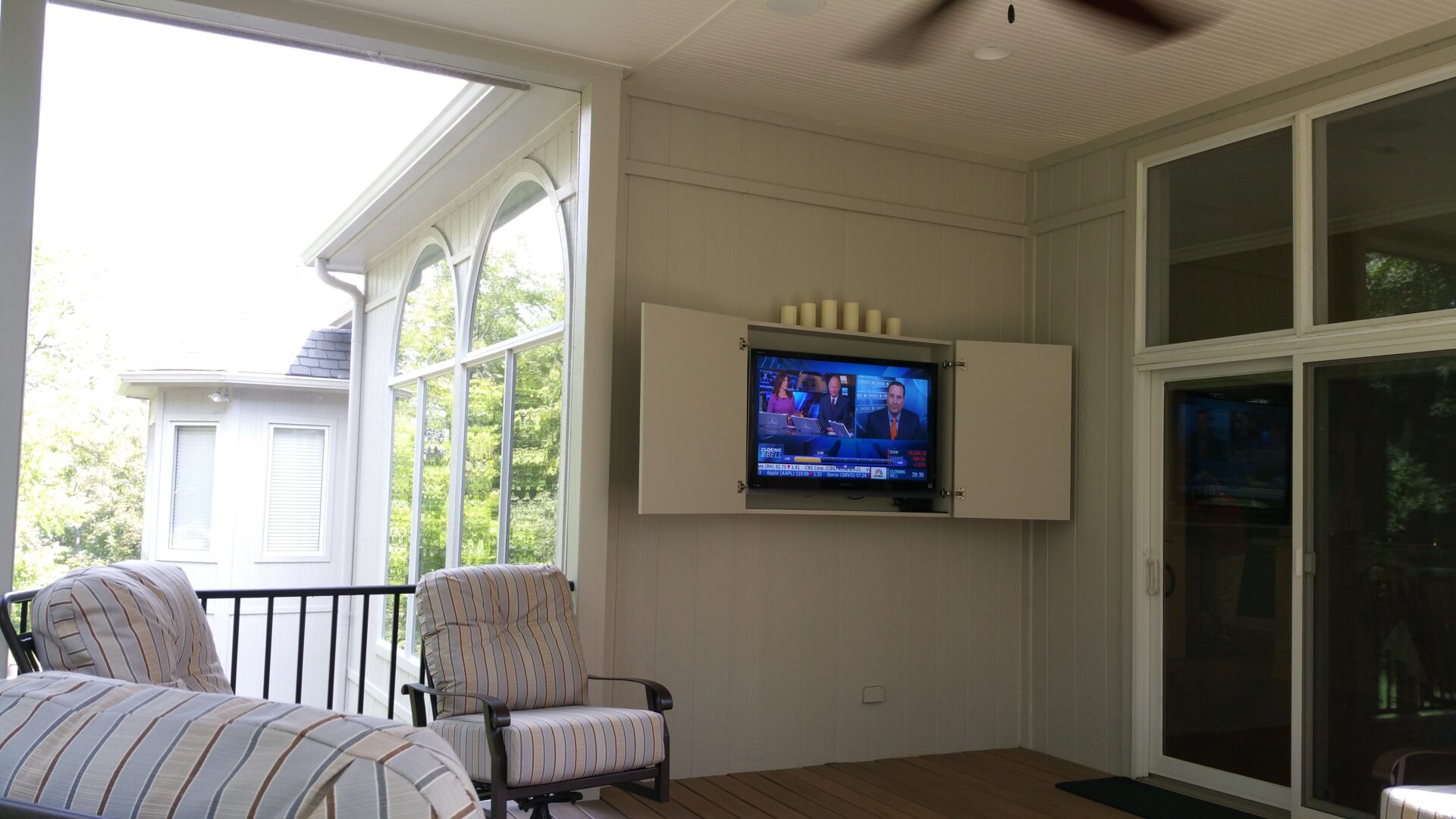 Cozy porch with TV and comfortable seating overlooking greenery.