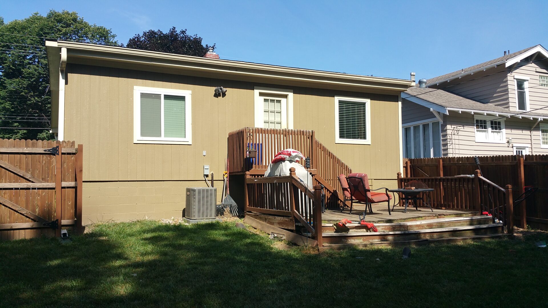 A small wooden deck with chairs outside a beige house.