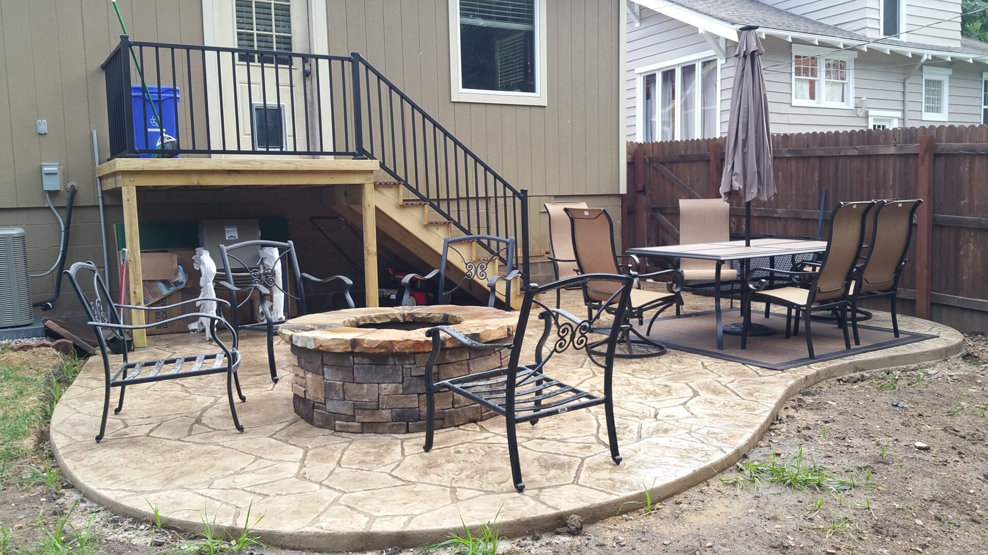 Outdoor patio with fire pit and metal chairs on stone flooring.