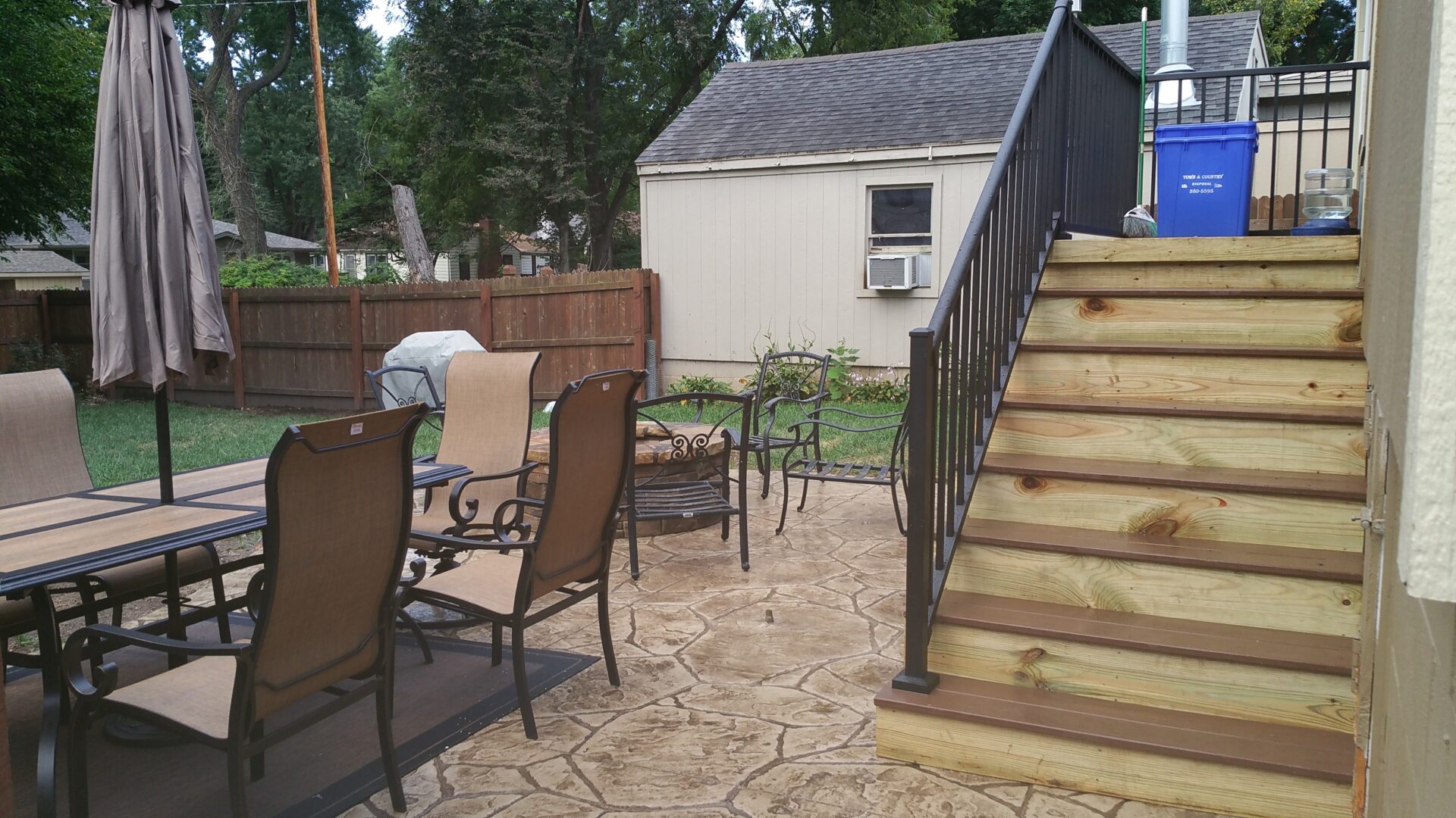 Outdoor patio with chairs and a staircase beside a small shed.