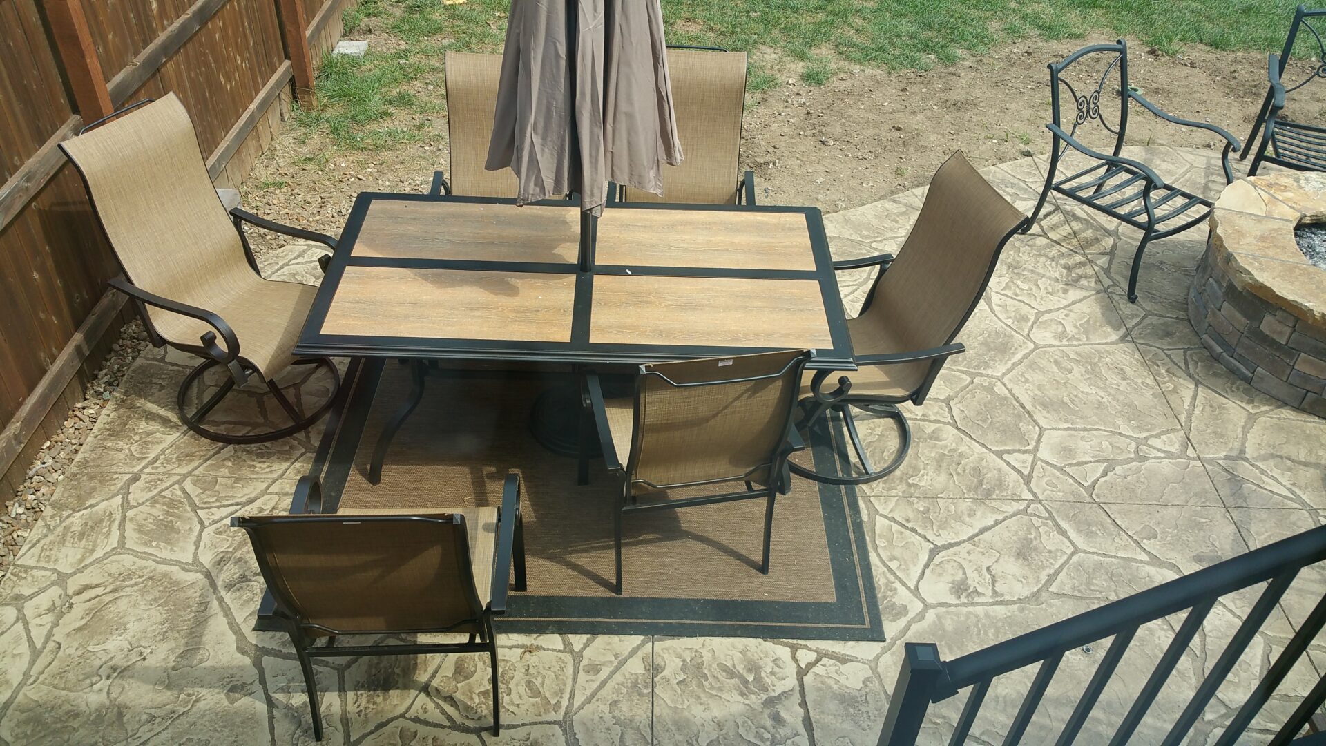 Outdoor patio set with glass-top table and four chairs on stone pavement.
