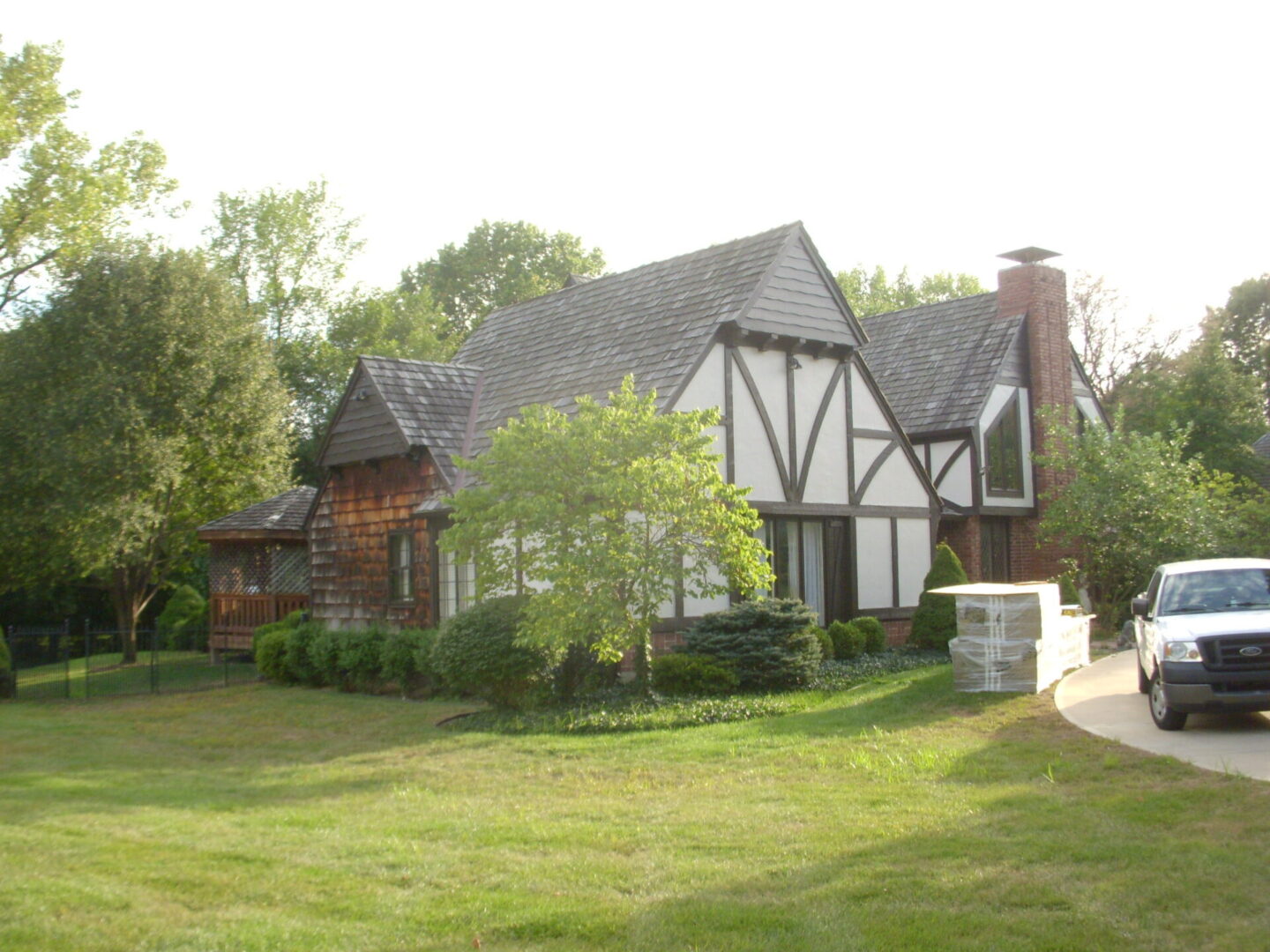 A quaint Tudor-style house with a large front lawn and trees.