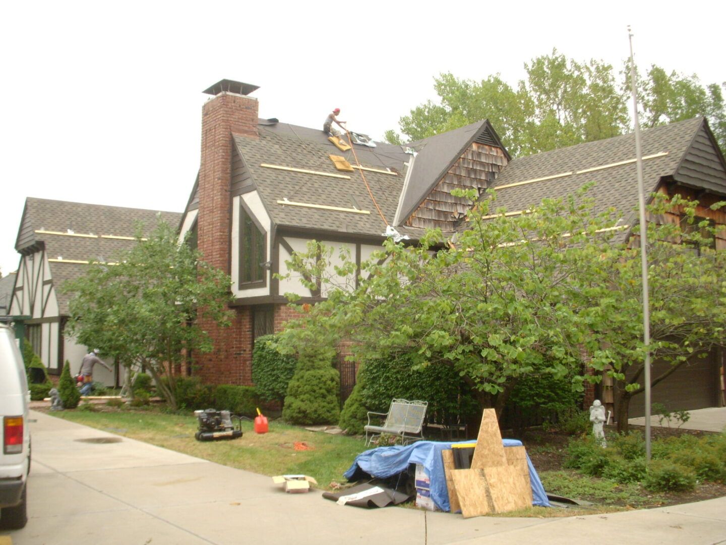 Workers repairing a residential roof with equipment and materials on the ground.