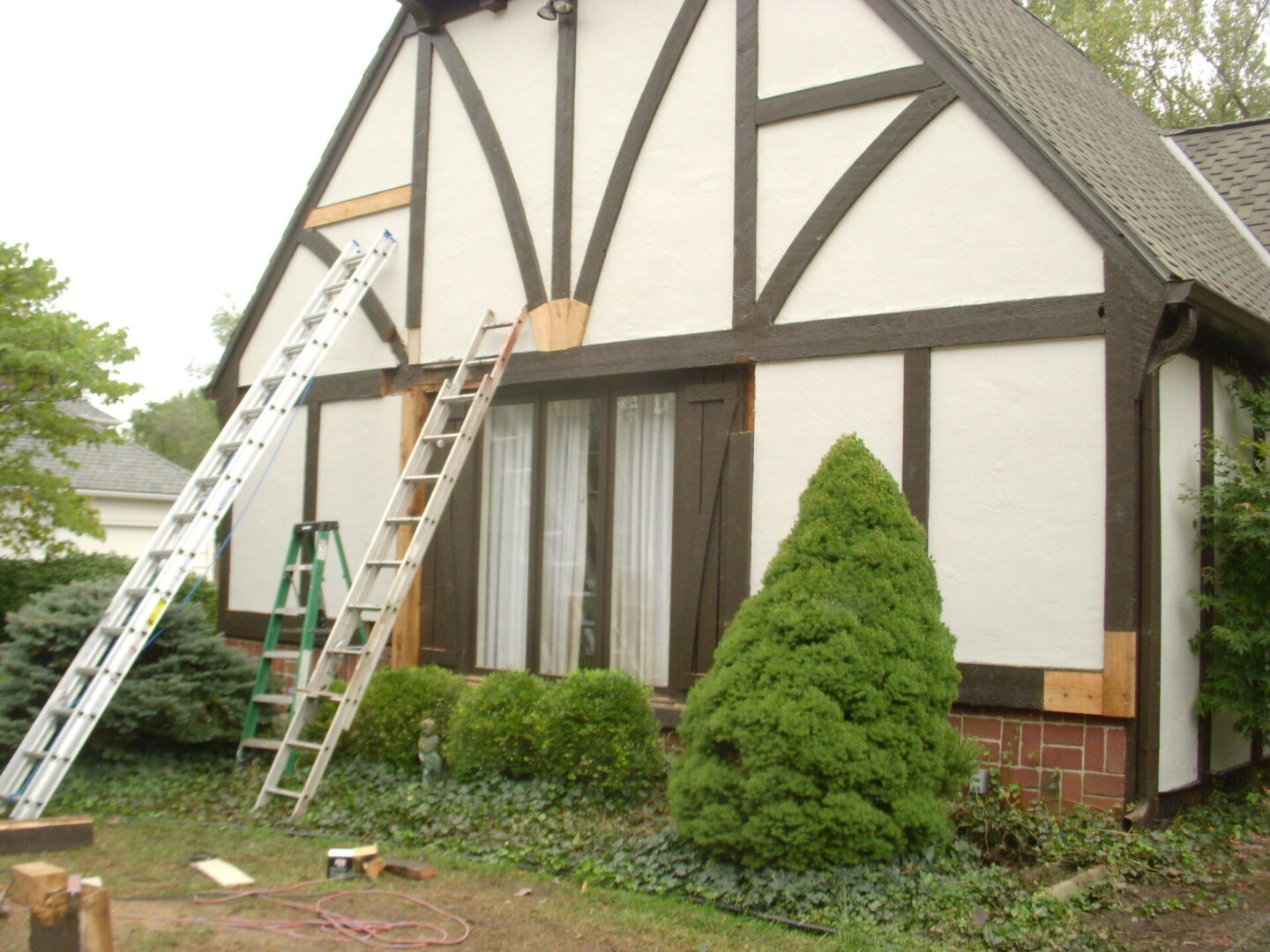Ladder leaning against a Tudor-style house with a trimmed bush nearby.